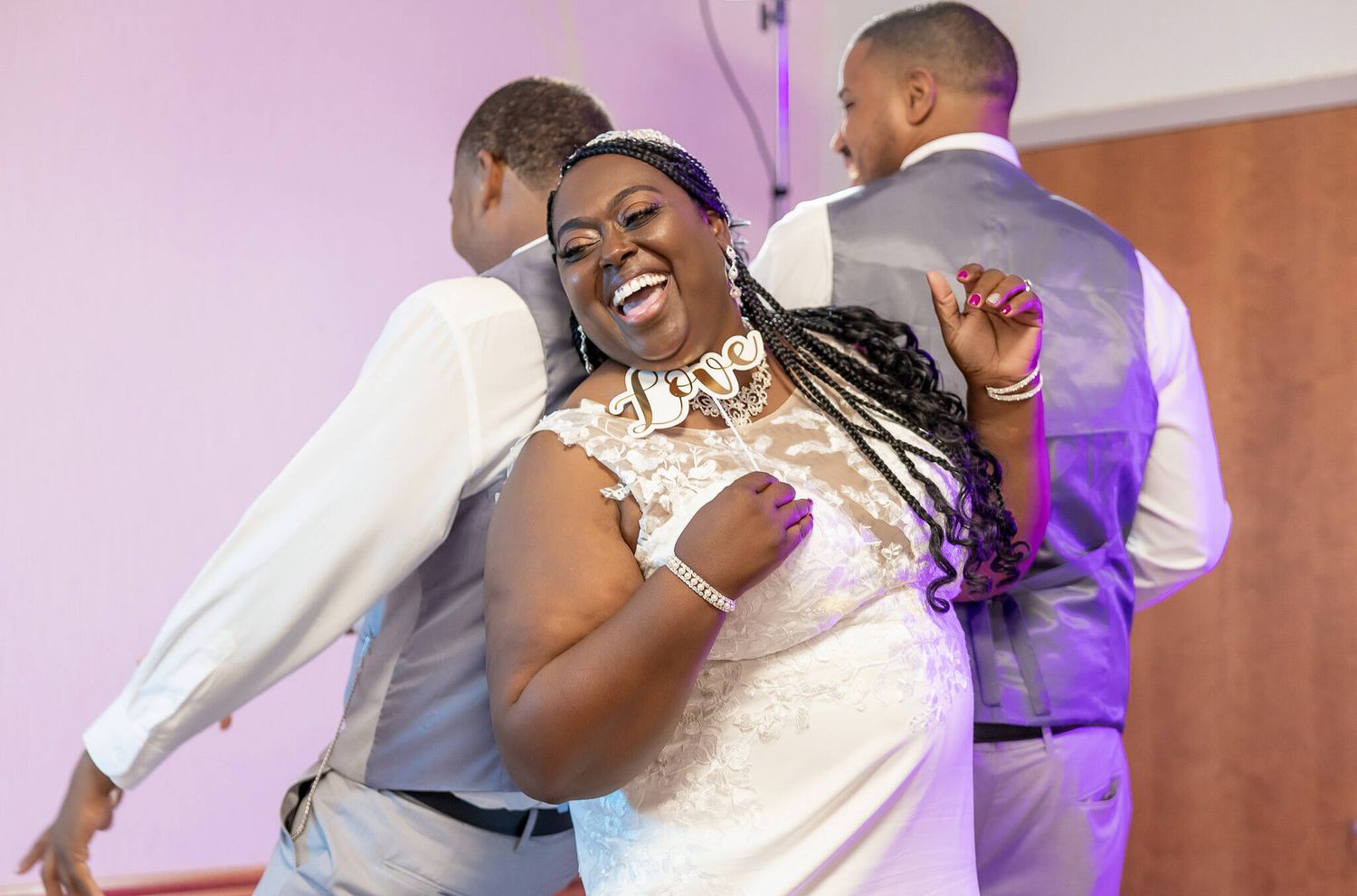 Wedding guests dance and celebrate together during a joyful reception with purple lighting and warm decor.