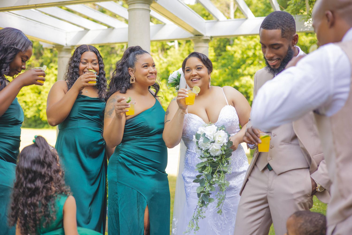 Wedding party in teal dresses and gray suits celebrates joyfully outdoors during summer reception.