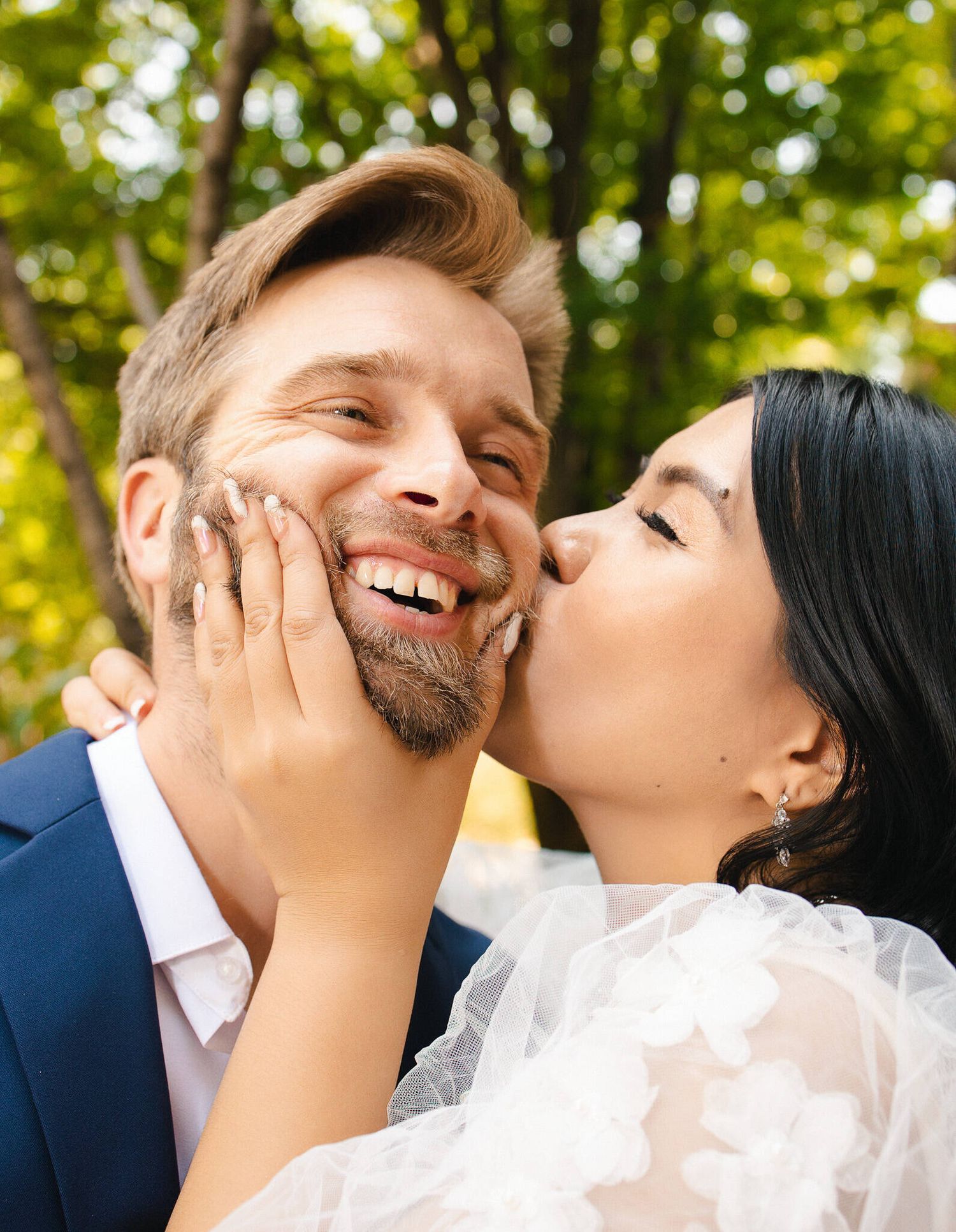 A happy couple shares a tender moment in a sunlit forest setting on their wedding day.