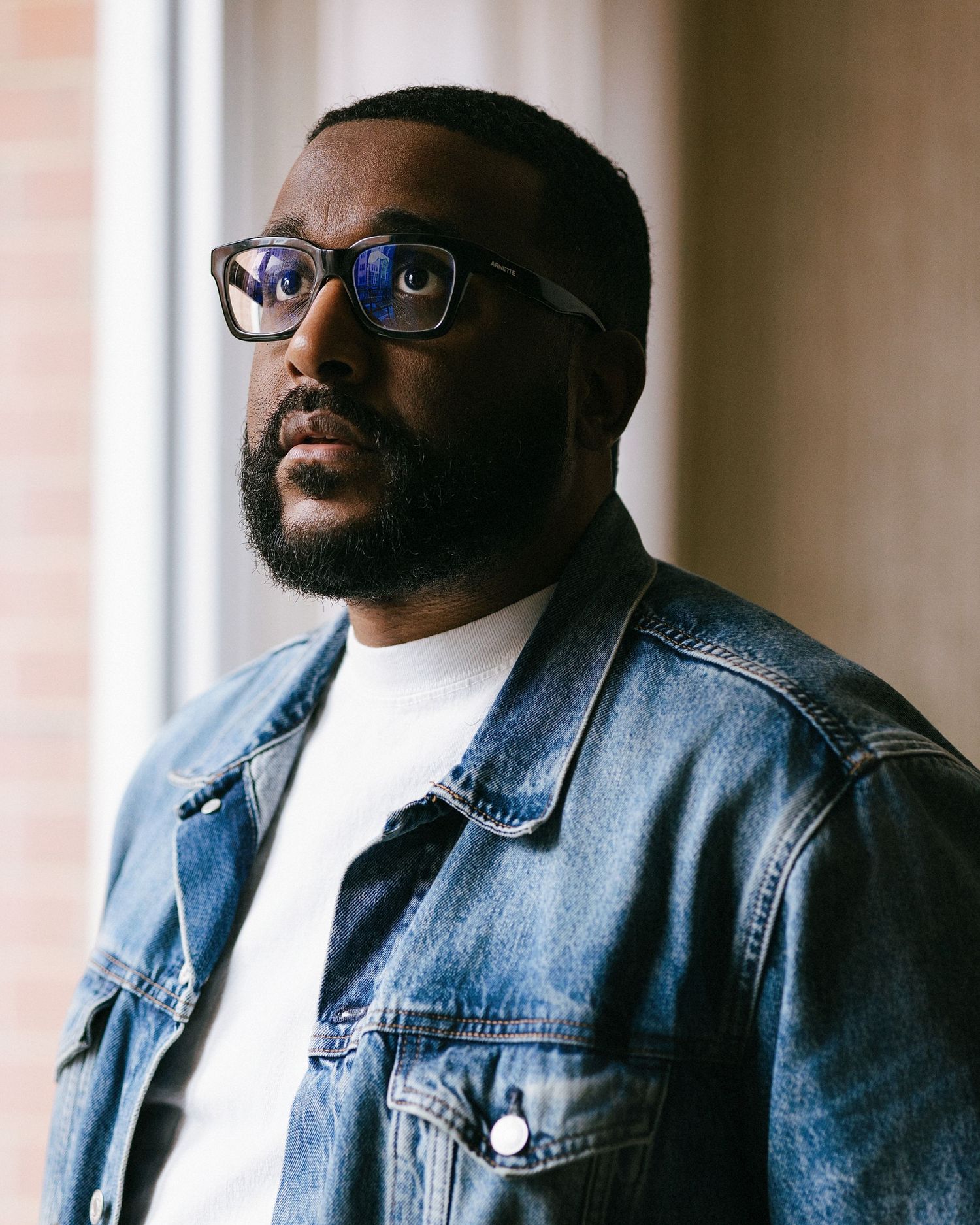 Person wearing glasses and denim jacket poses near window in moody lighting with multiple profile angles shown.