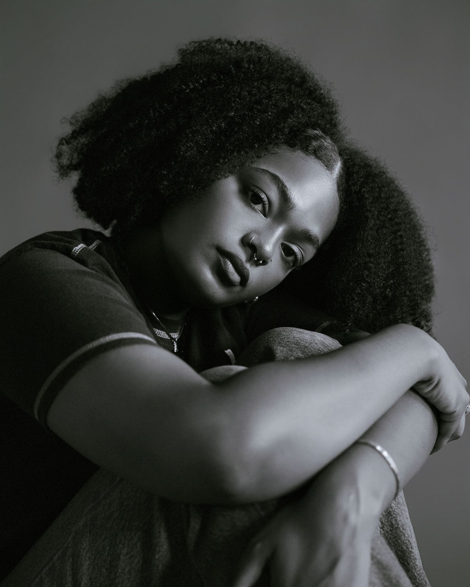 Artistic black and white portrait series showing a person with natural afro hair in contemplative poses against dark background.