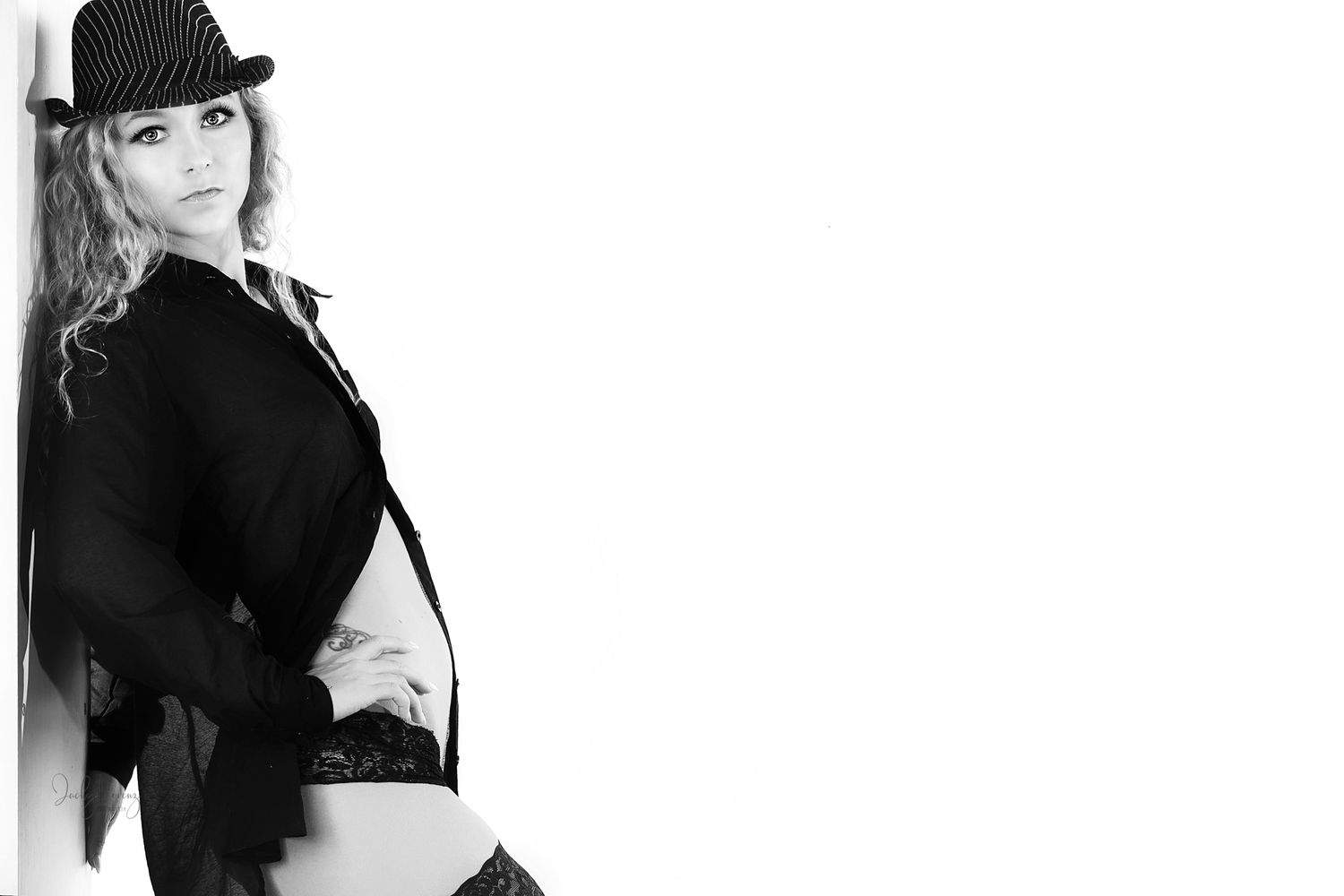 Professional fashion model poses in black outfit and hat against white background for studio photoshoot.