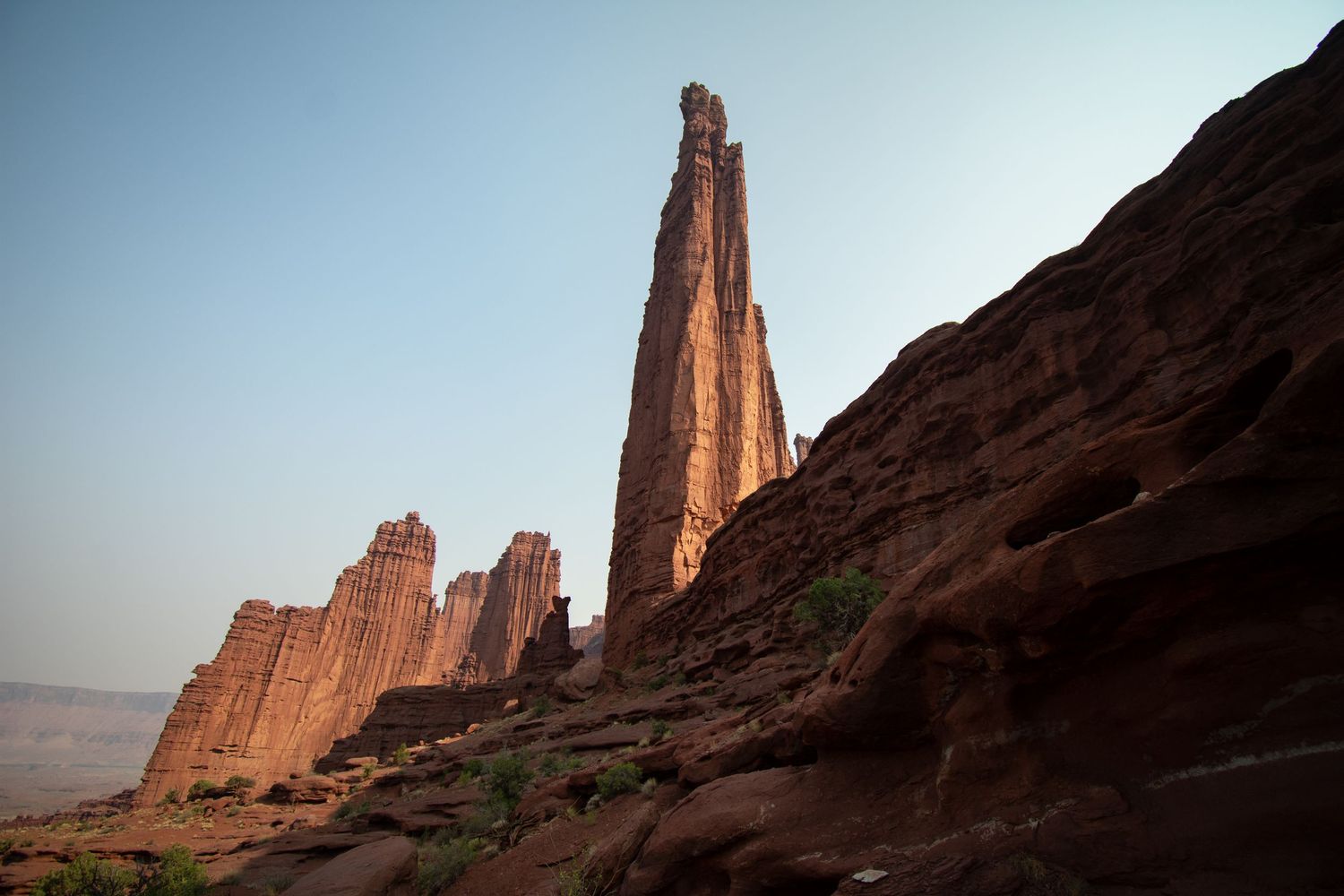 A view looking upwards at one of the tallest spires of the Fisher Towers area, with the wall of a sandstone cliff dividing the frame.