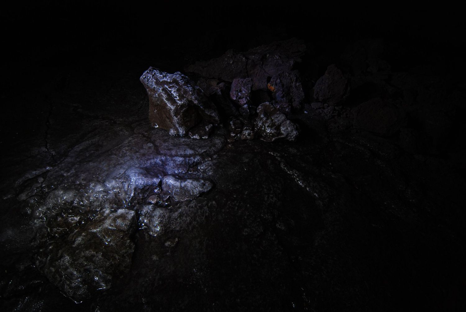 A dark photo from inside an igneous lava-tube cave with a rock formation lit by a single faint source of light.