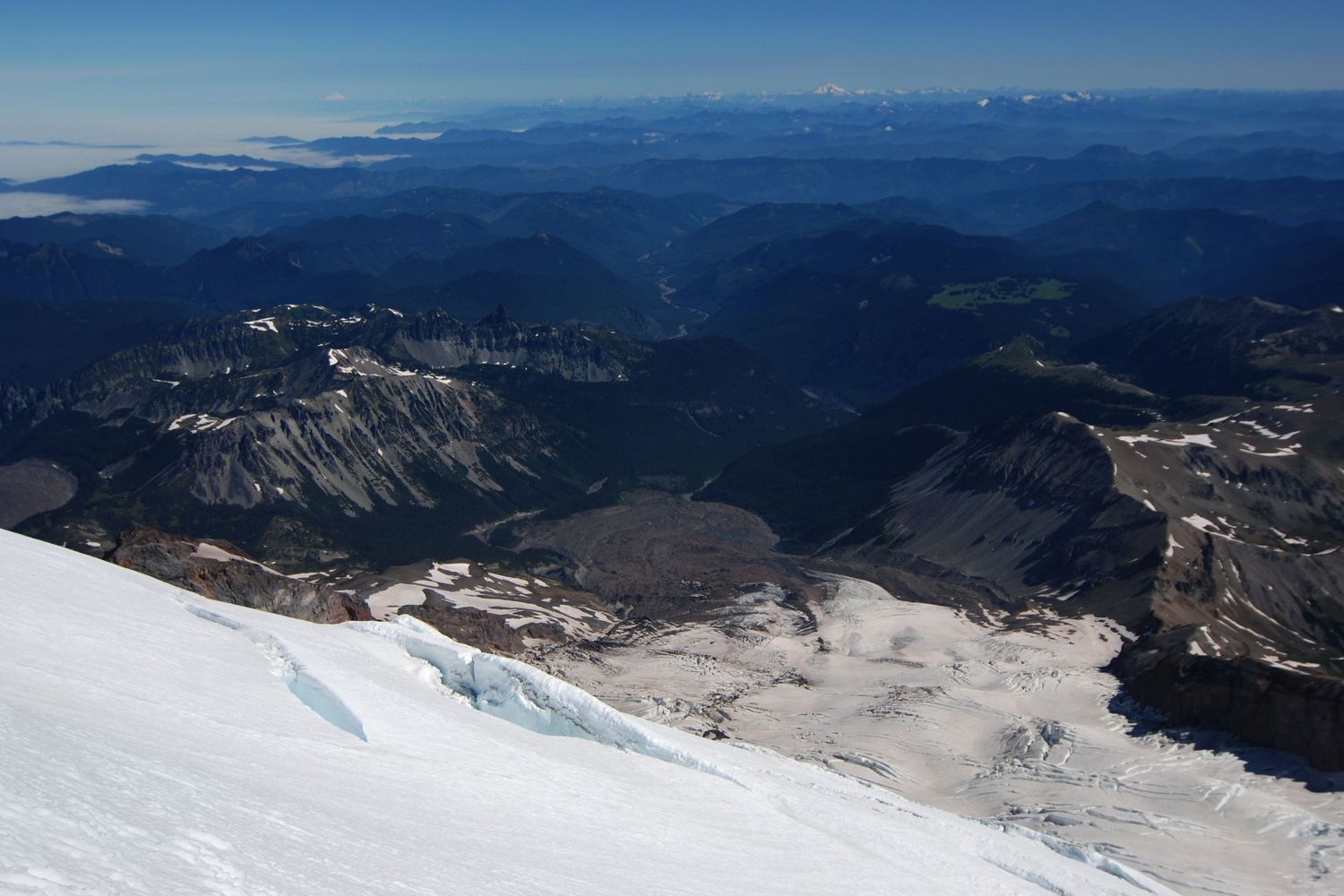 A view looking north from high on the Winthrop glacier on Mount Rainier. A cloud bank and the North Cascades are in the vast distance.
