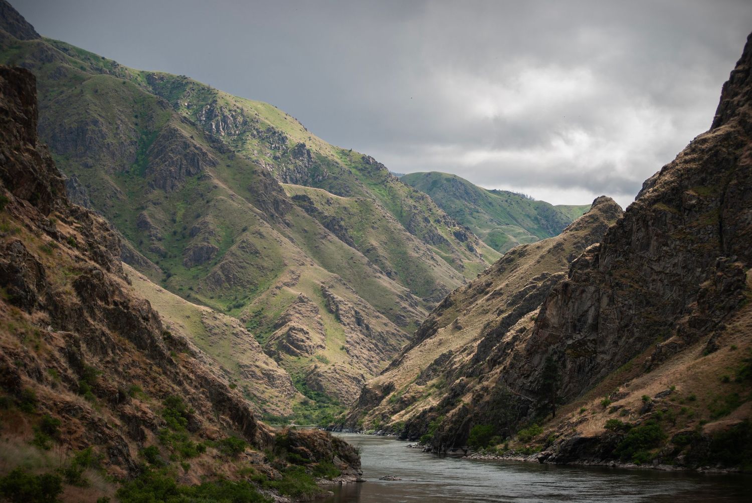 A photo of Hells Canyon and the Snake river that runs through it, on an overcast day with light hitting the eroded riverside cliffs.