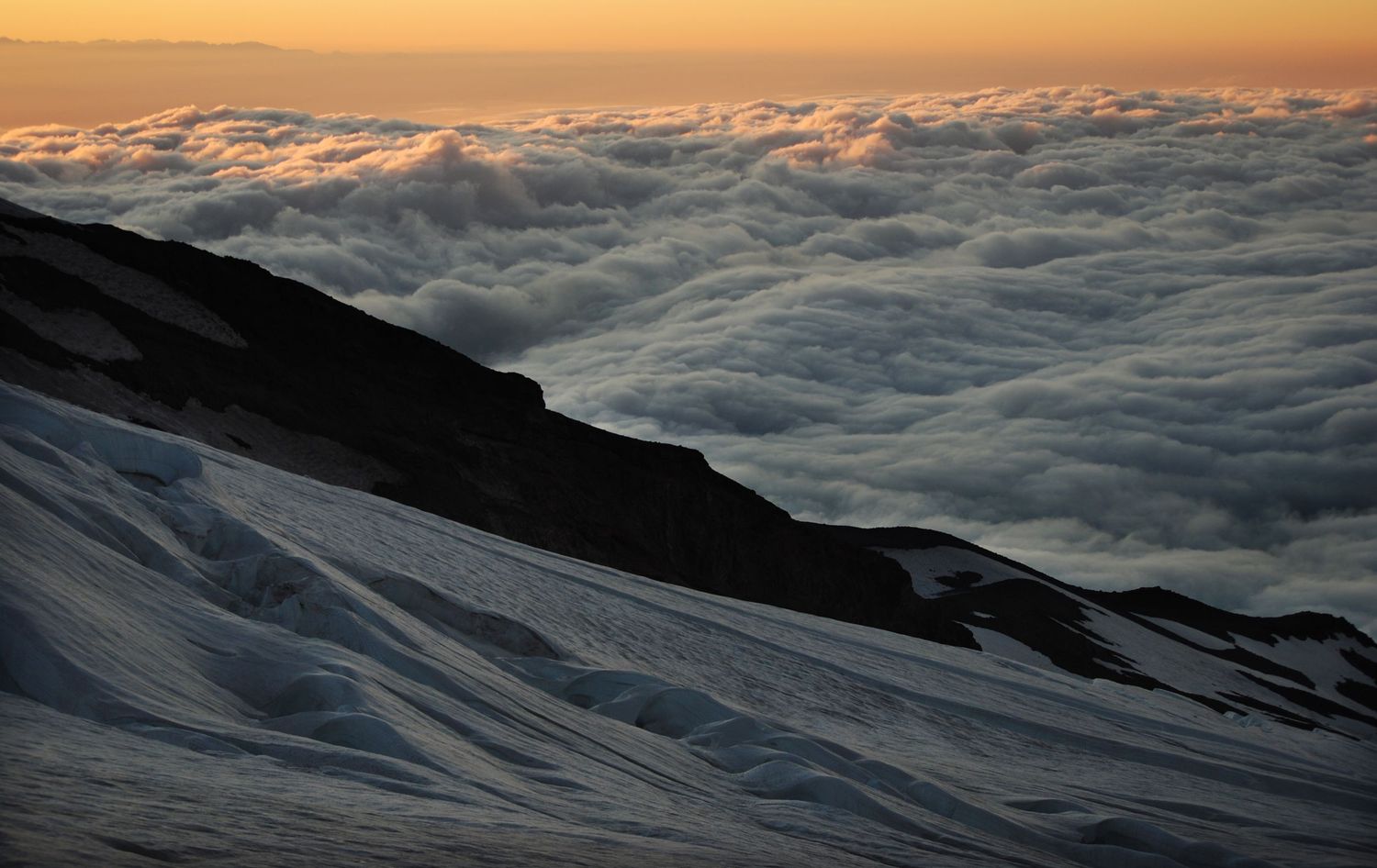 A high altitude view from near Camp Schurman of the Winthrop glacier sliding down above a sea of clouds lit by sunrise on Mount Rainier.