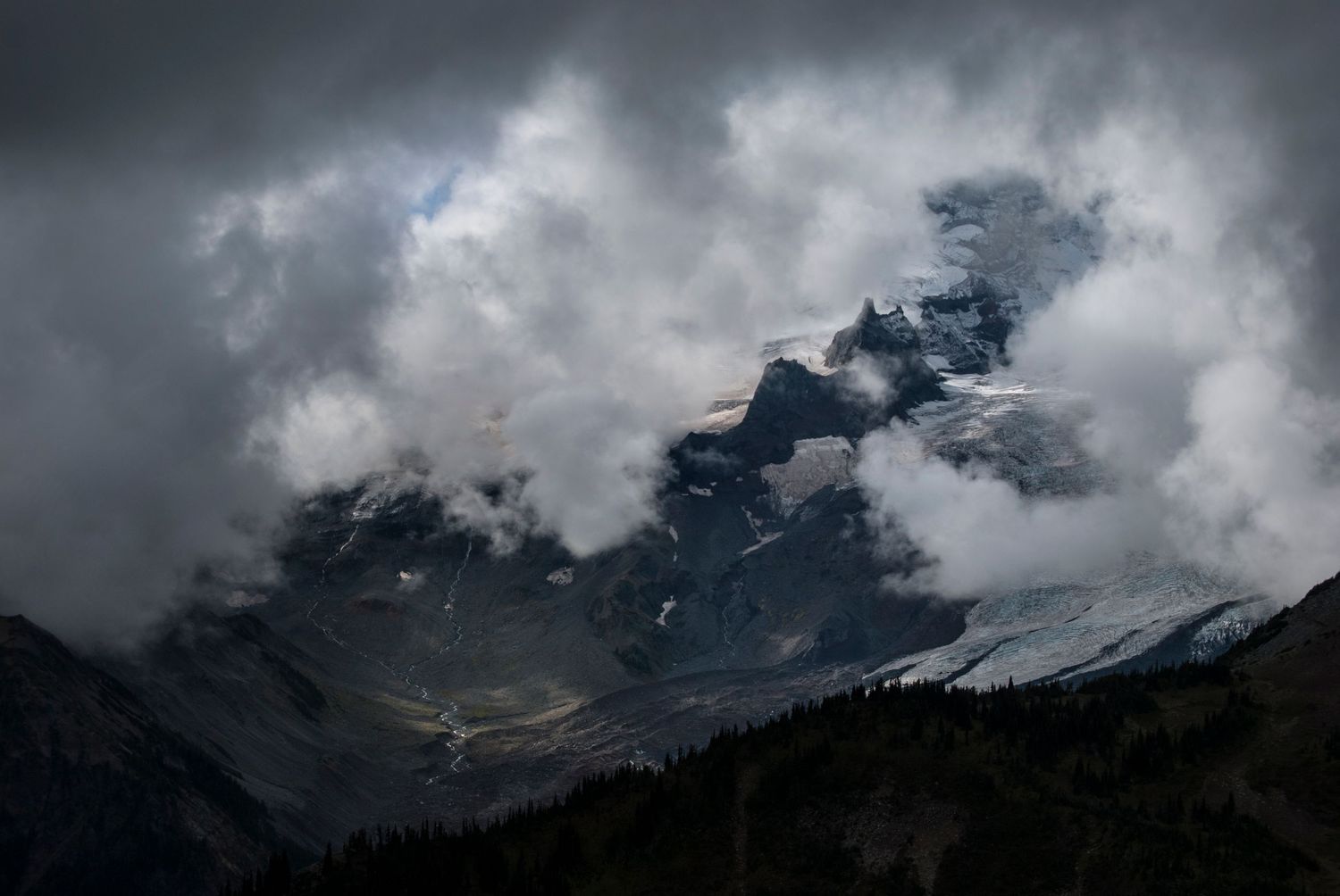 A veil of clouds encroaches upon a massive valley carved by the Emmons glacier on the north side of Mount Rainier.