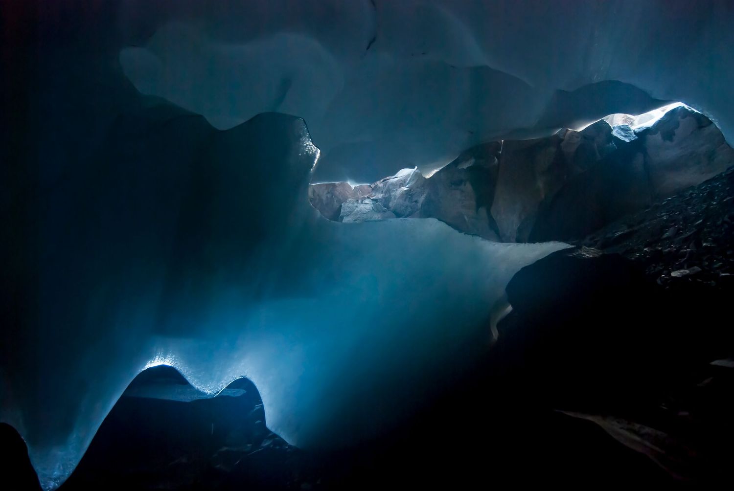 A blue steam cave on the summit of Mount Rainier carved out of ice with the rock below leaving only several feet of open space.