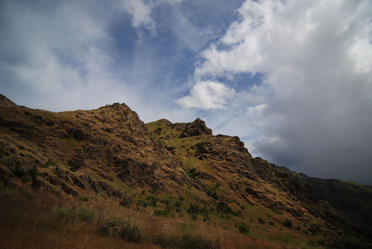 A view looking up at brown river-side cliffs along the Snake river in Hells Canyon, with clouds on either side of an opening to blue sky.