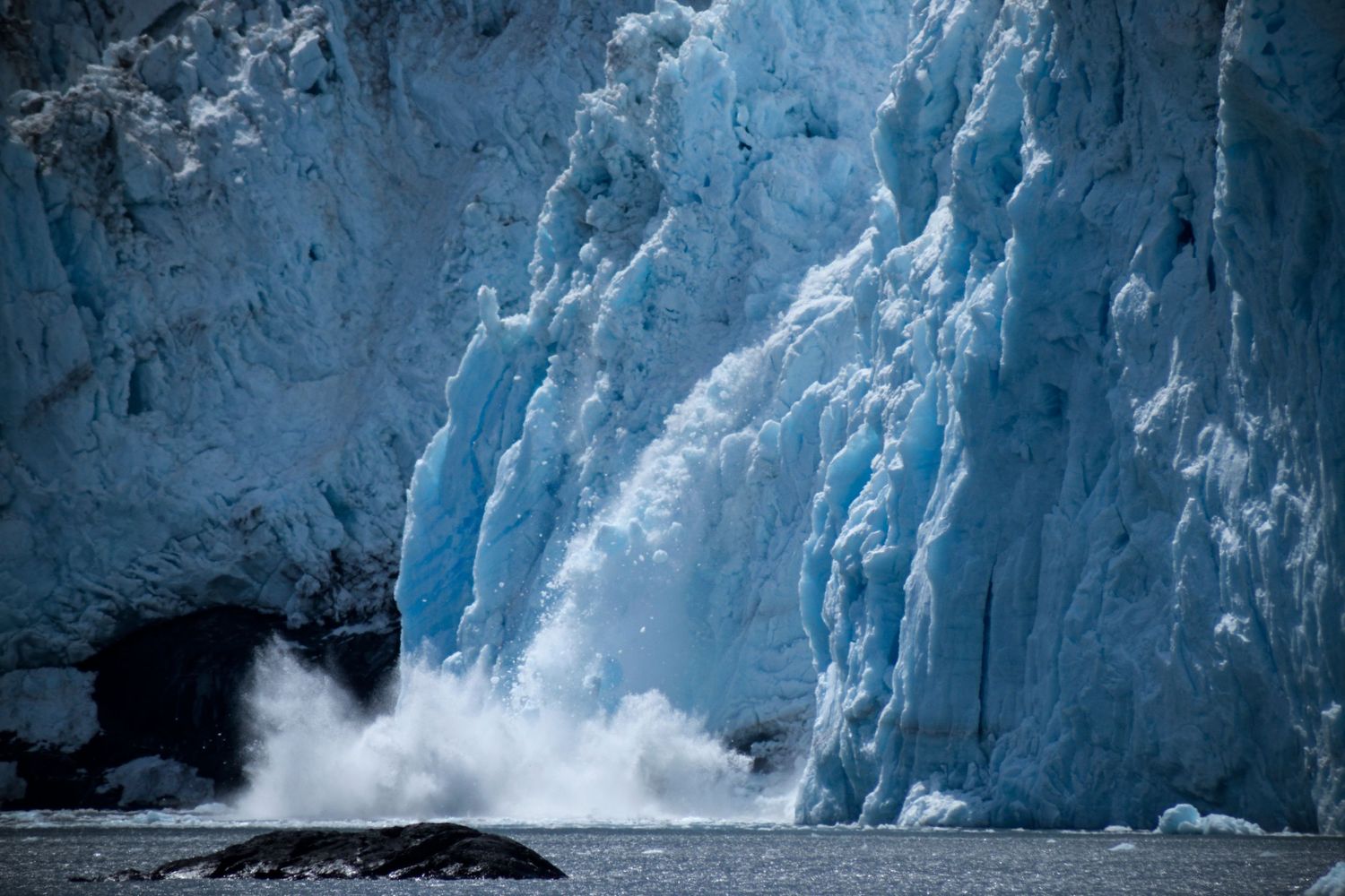 Calving glacial ice falling into the sea, a splash frozen in the photo.