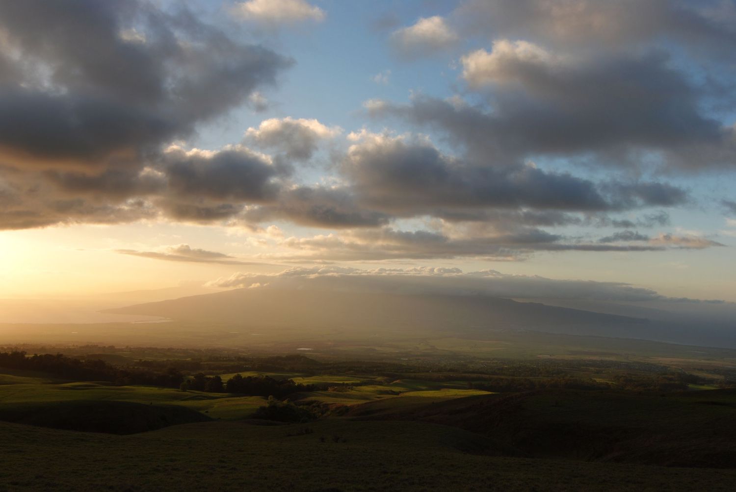 A soft golden sunset looking across Maui from east to west, amidst large open ranchlands.