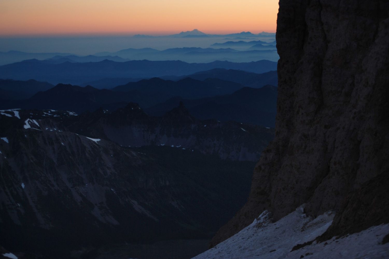 A high elevation view of tall cliffs at sunset from near Camp Schurman on Mount Rainier, peachy sky and dark mountains in foreground.