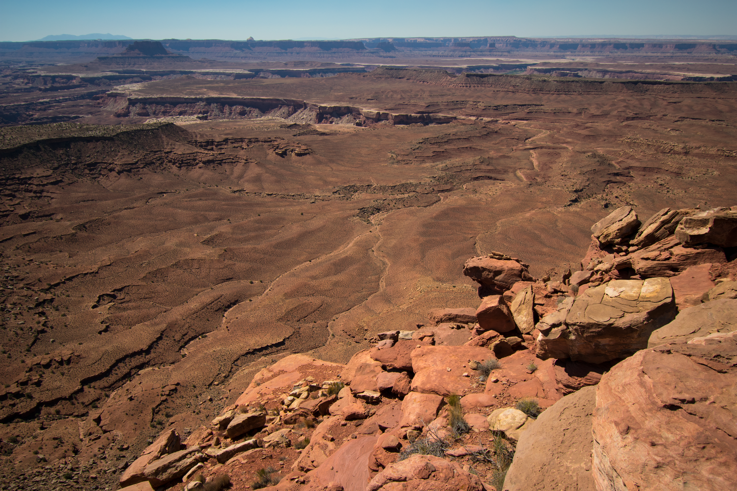 A high up view of a desolate part of Canyonlands National Park with brown and red canyons and sandstone rock in the lower right foreground.