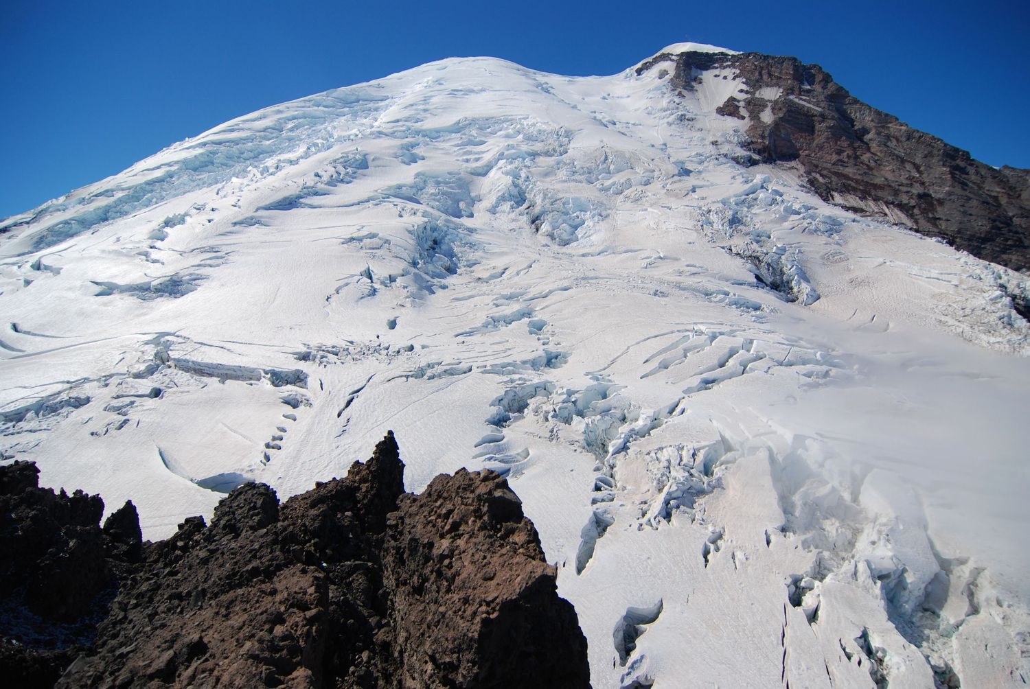 A view towards the summit of Mount Rainier from Steamboat Prow, showing the huge Winthrop and Emmons glaciers and blue sky above.