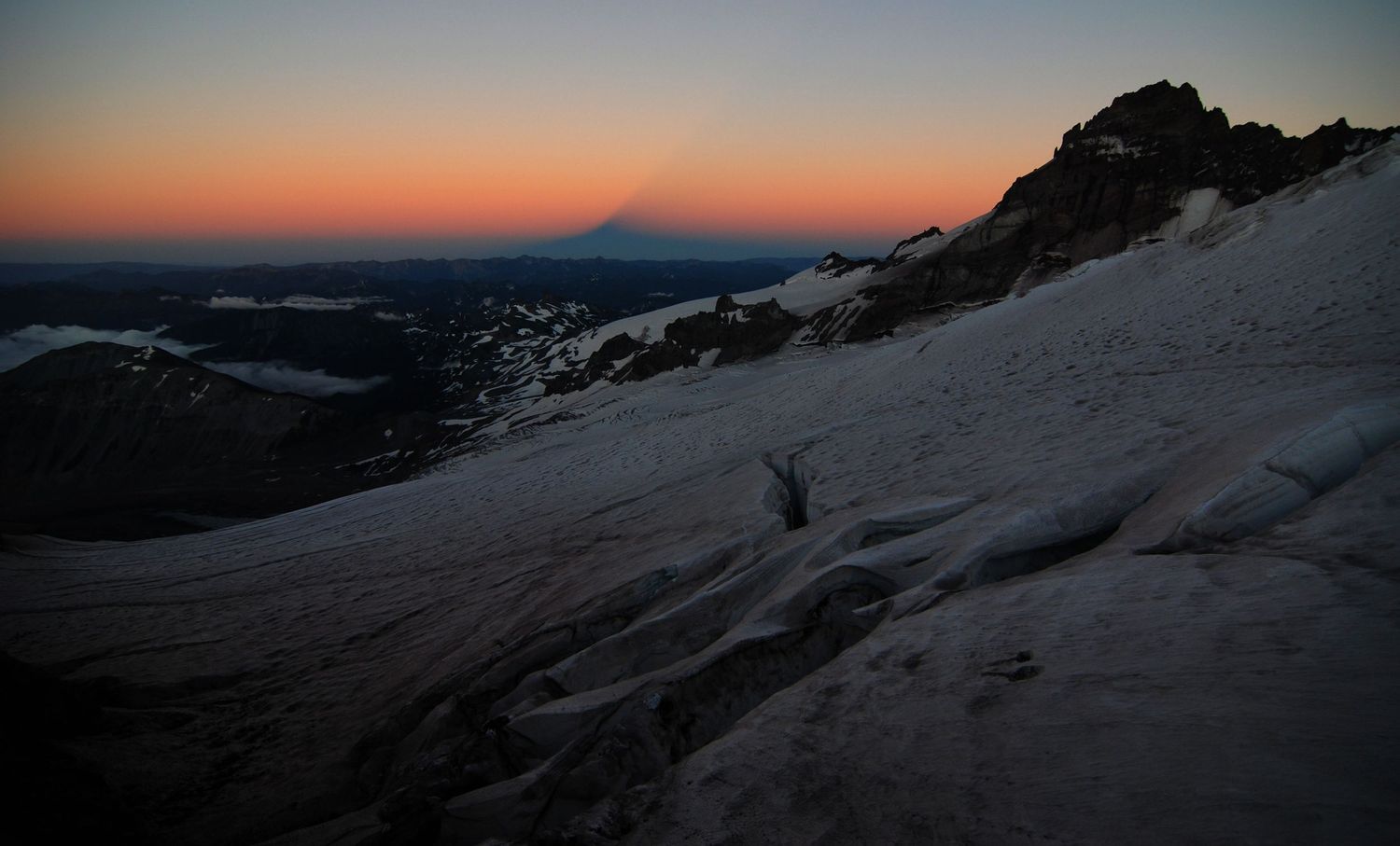 A peachy sunset view from the Emmons glacier near Camp Schurman with Little Tahoma on right right and the shadow of the mountain in the sky.