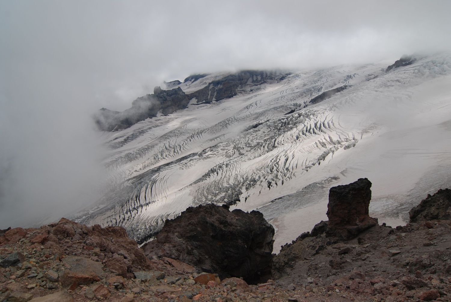 A view through a portal of clouds of the Emmons glacier on the north side of Mount Rainier, seen from Mt. Ruth, a rocky climbers trail.
