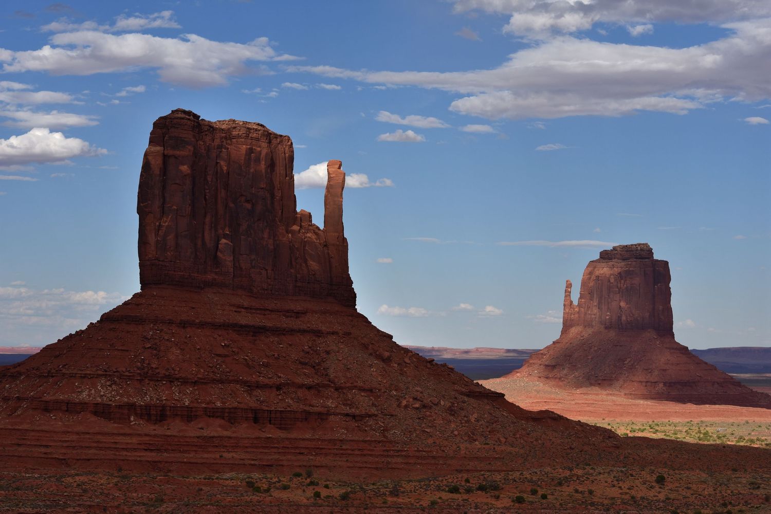 The iconic 'Mitten' buttes of Monument Valley; the foreground butte is in deep shadow while the distant butte is illuminated by sun.