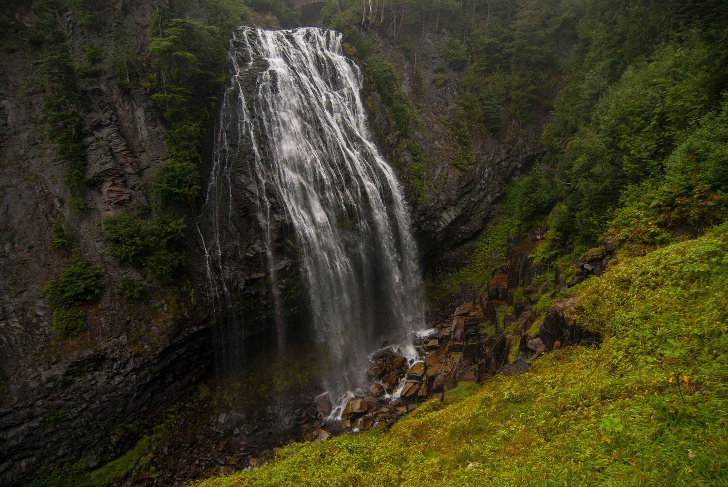 Spray Falls, a large waterfall in a valley in Mount Rainier National Park, the falls is wide and the surrounding area is verdant green.