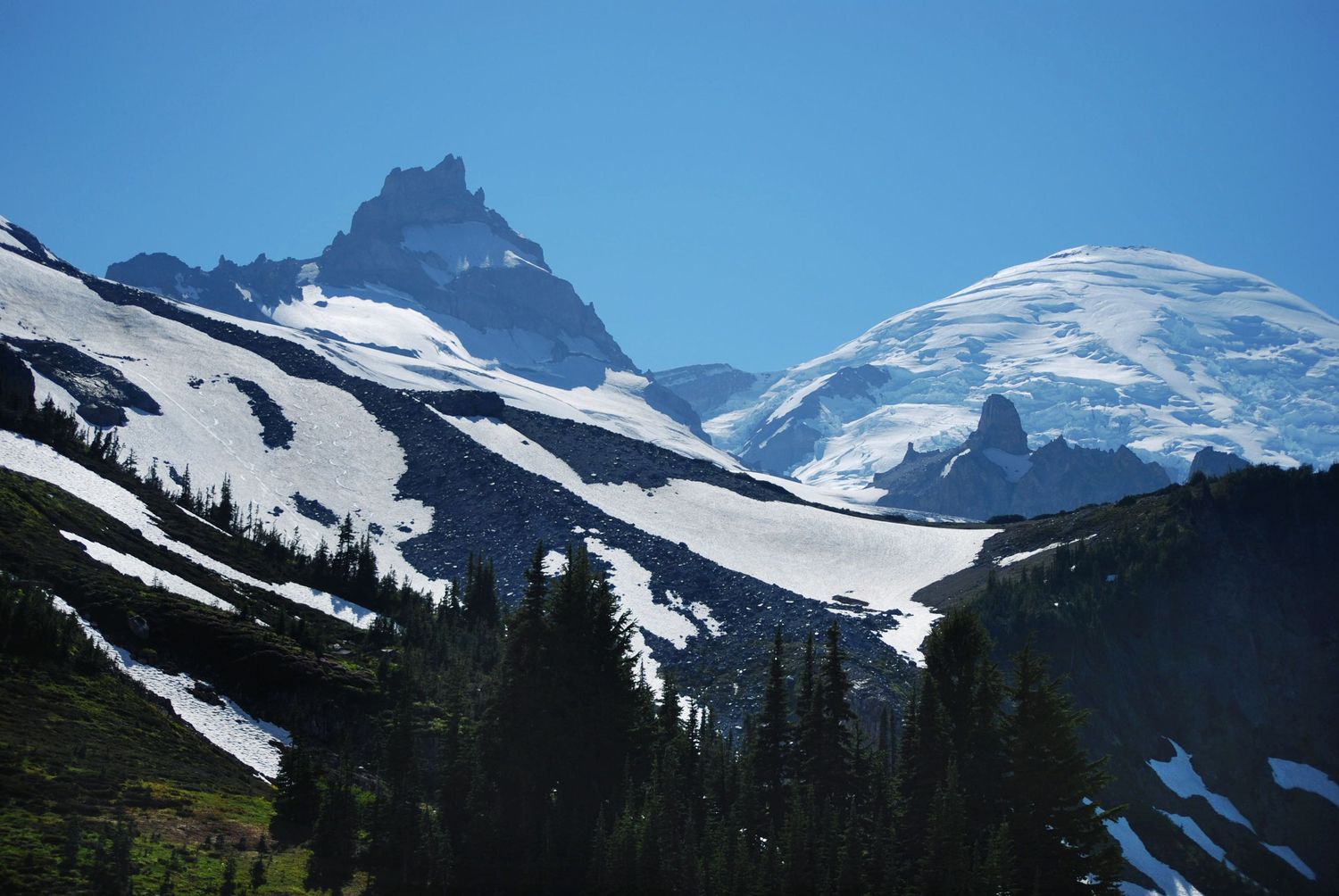 A summertime view of Little Tahoma and the summit of Mount Rainier, from an angle that places the summit lower with a bright snowy ridge.