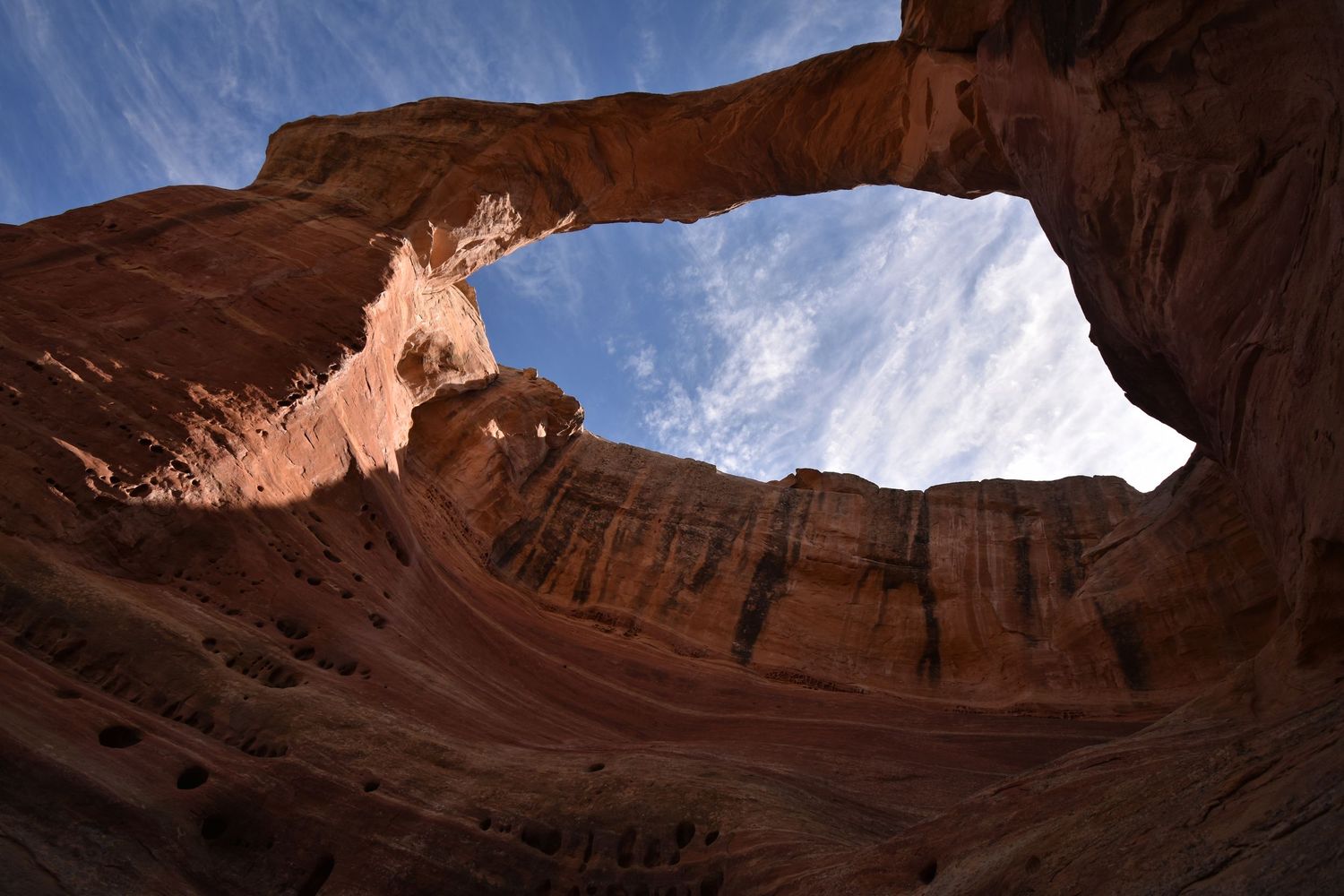 A large sandstone arch in Colorado National Monument, seen from below on a mostly clear summer day.