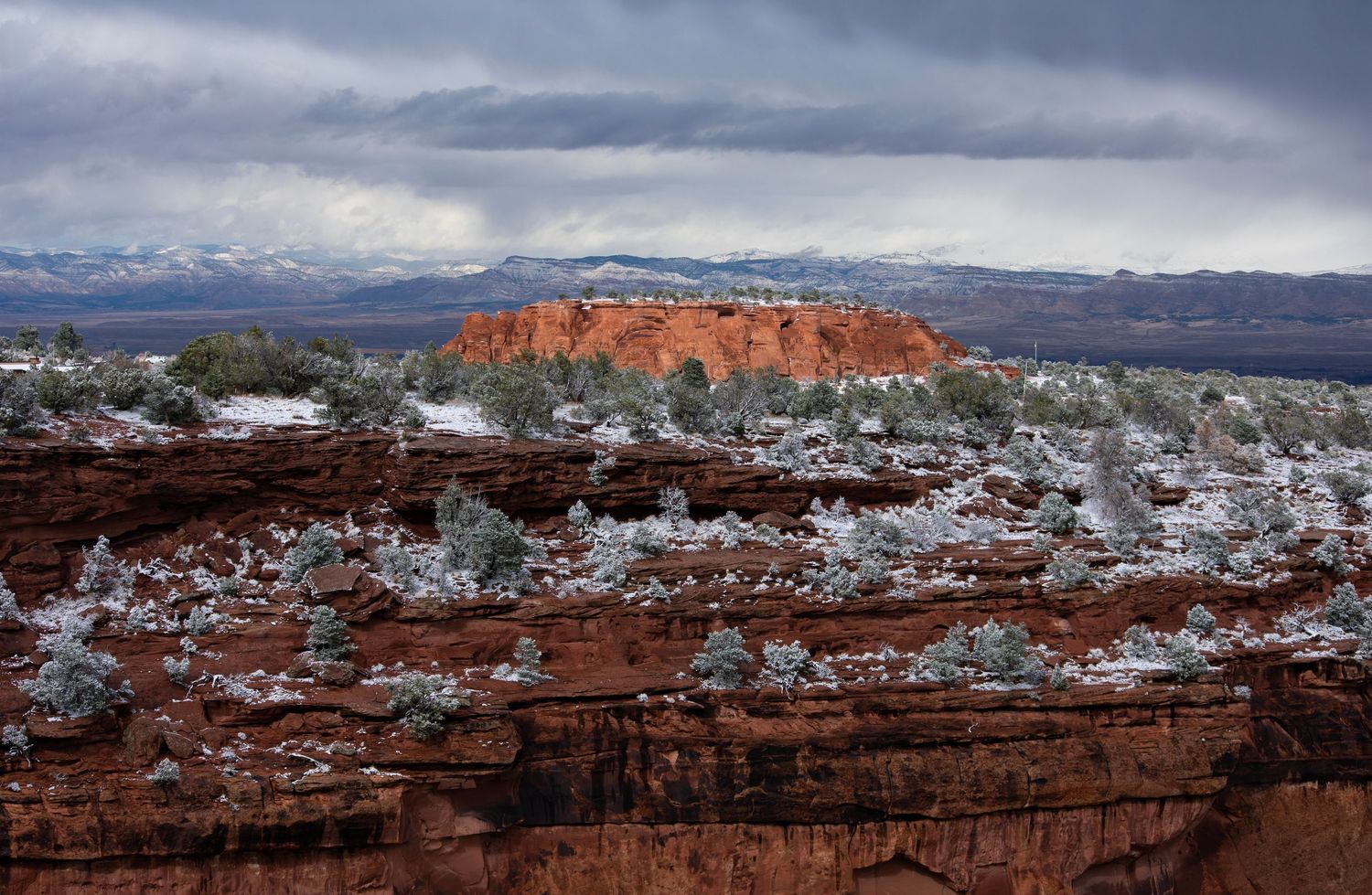 Colorado National Monument on a winter day with snow decorating sandstone cliffs in front of a very long view to the valley beyond the park.