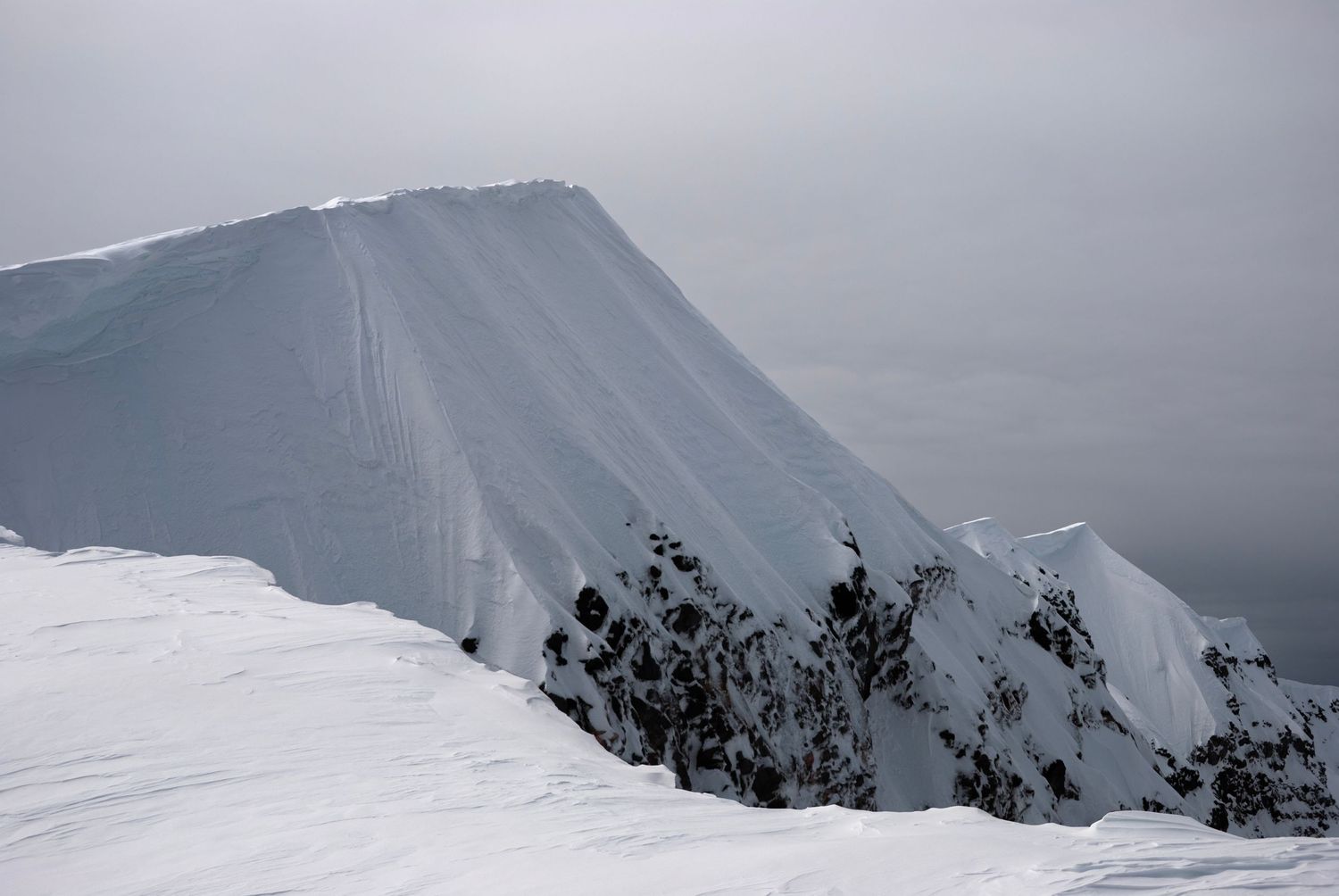A closeup of a tall ridge that is part of the summit rim of Mount St. Helen's crater, covered in snow on a cloudy day.