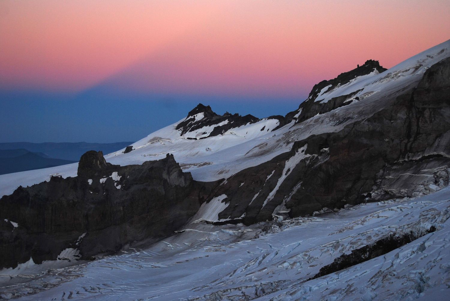 A glaciated view from high on Tahoma that shows a unique phenomenon: the shadow the mountain carves out of the pink sky itself at sunset.