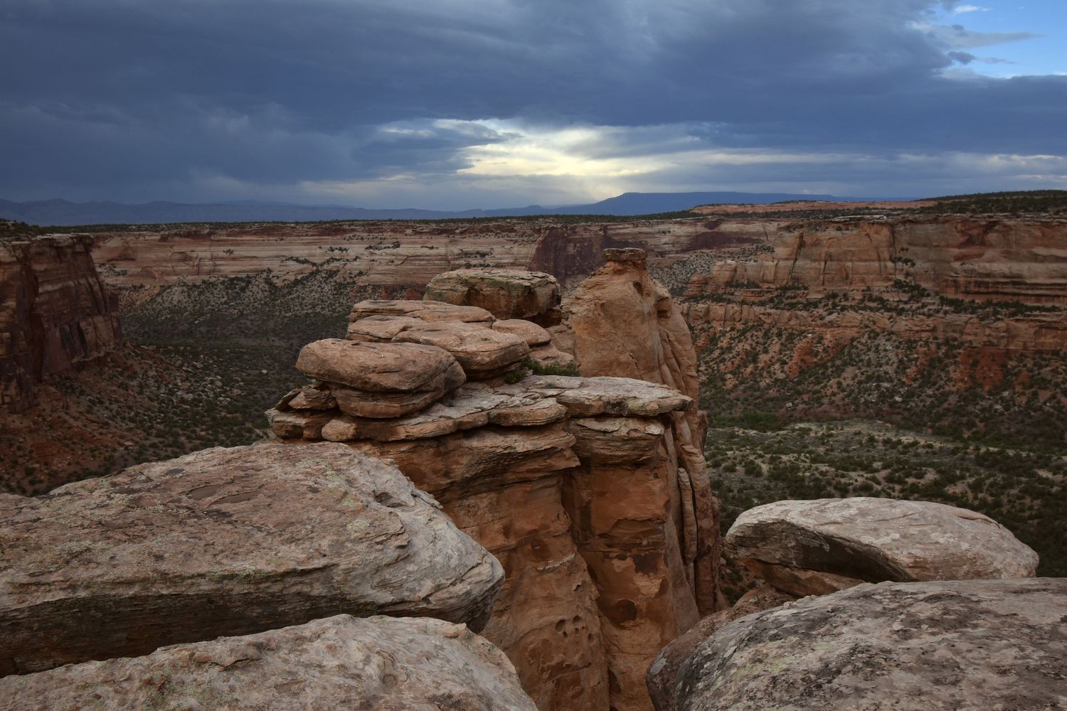 A moody grey sunset looking down at the tops of tall sandstone formations on the edge of a large canyon in Colorado National Monument.