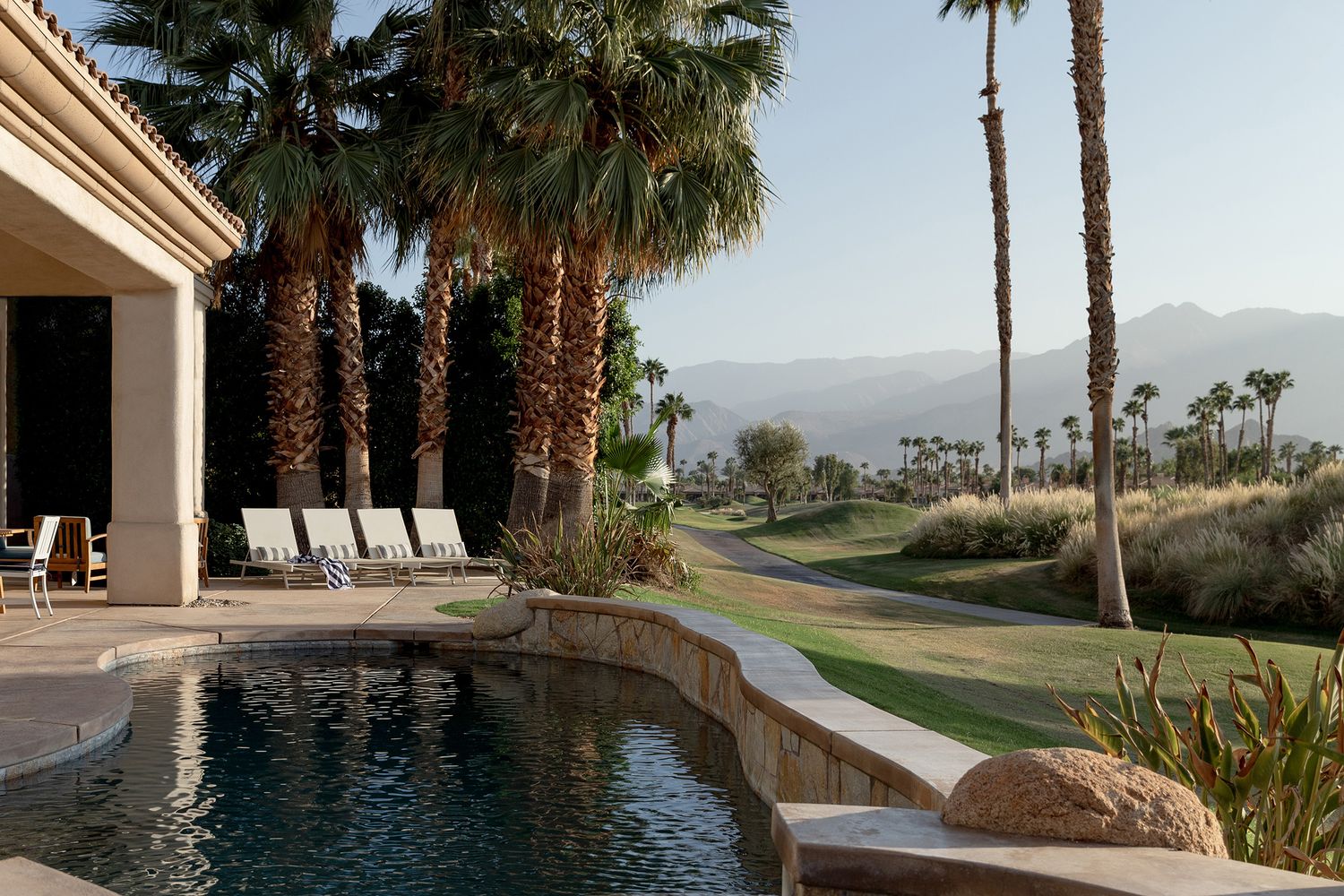 Luxury resort poolside with palm trees and mountain views in the desert landscape.