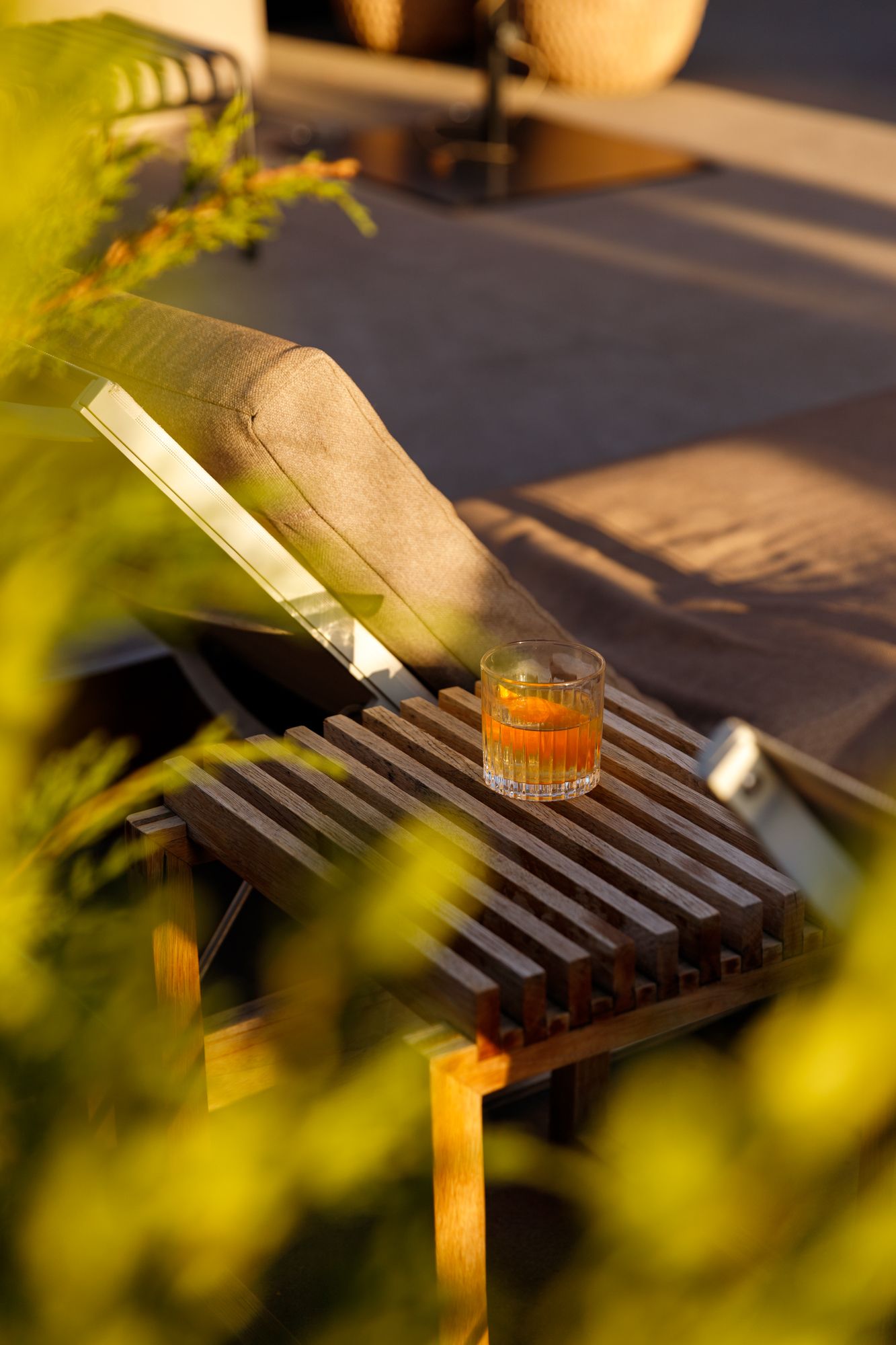 Amber cocktail in crystal glass on wooden lounge chair side table at sunset.