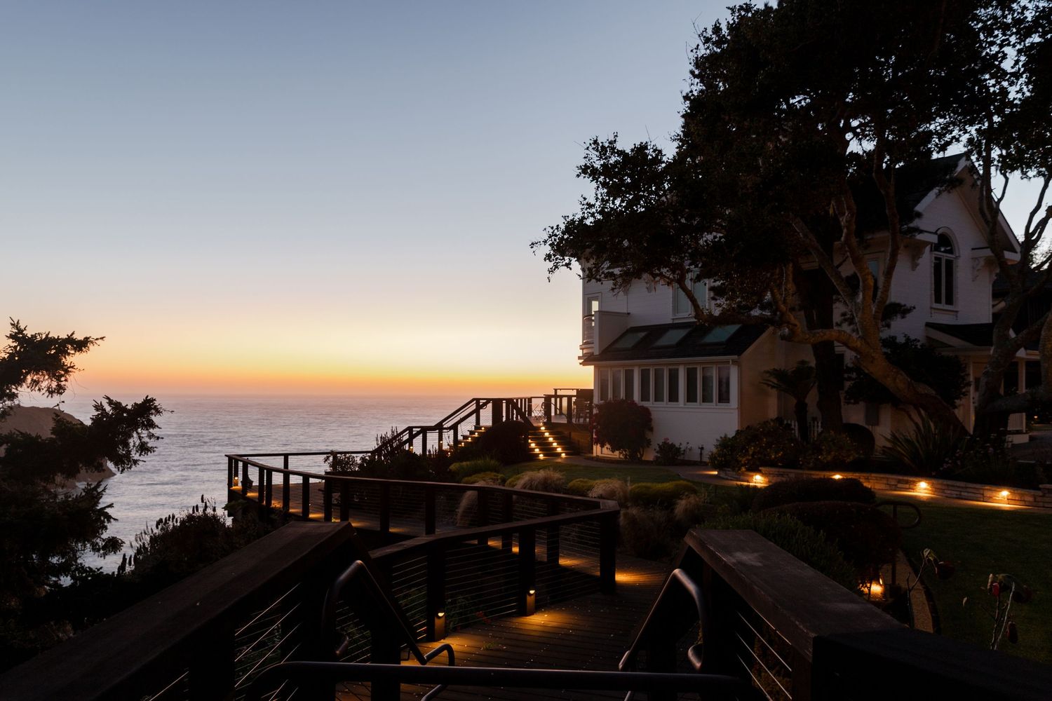 Coastal cliffside home with illuminated deck stairs at sunset. Documentary style photographer. Professional photographer Colorado.