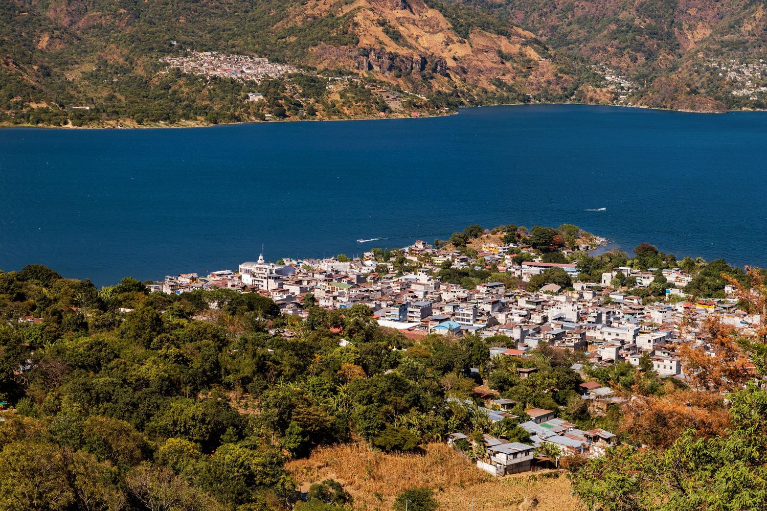 Panoramic coastal view of a Mediterranean town nestled in hills beside blue waters.