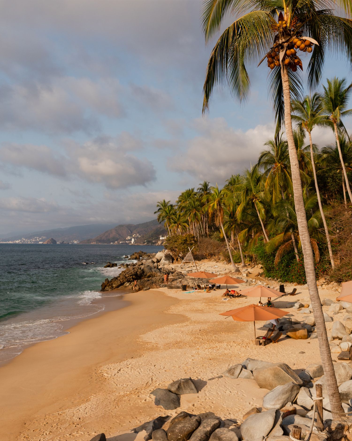 Palm-lined tropical beach with golden sand and rocky outcrops stretching along the coastline.
