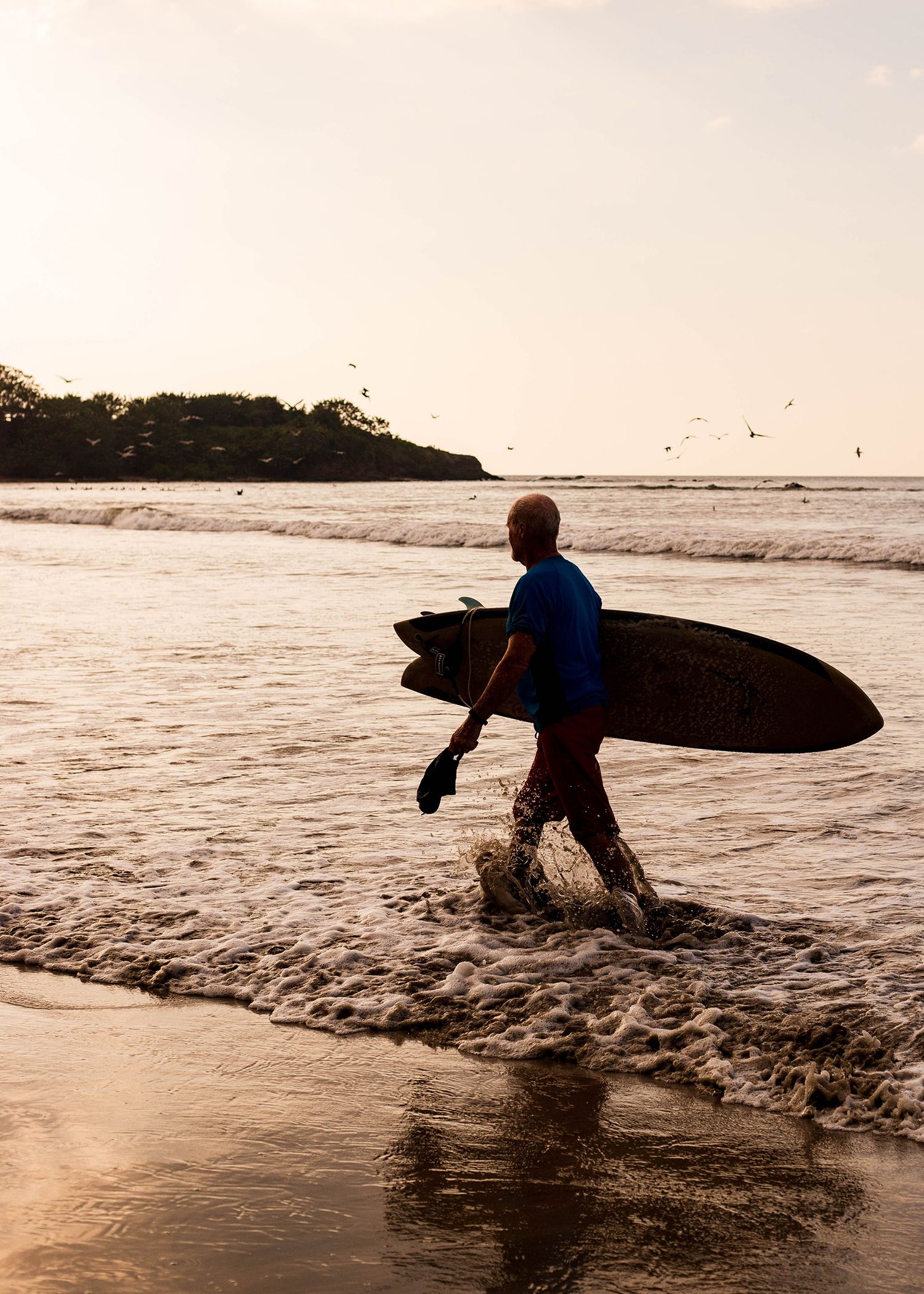 Silhouette of surfer carrying surfboard into ocean waves at sunset. Image by commercial photographer in Colorado Adrian Kahn.
