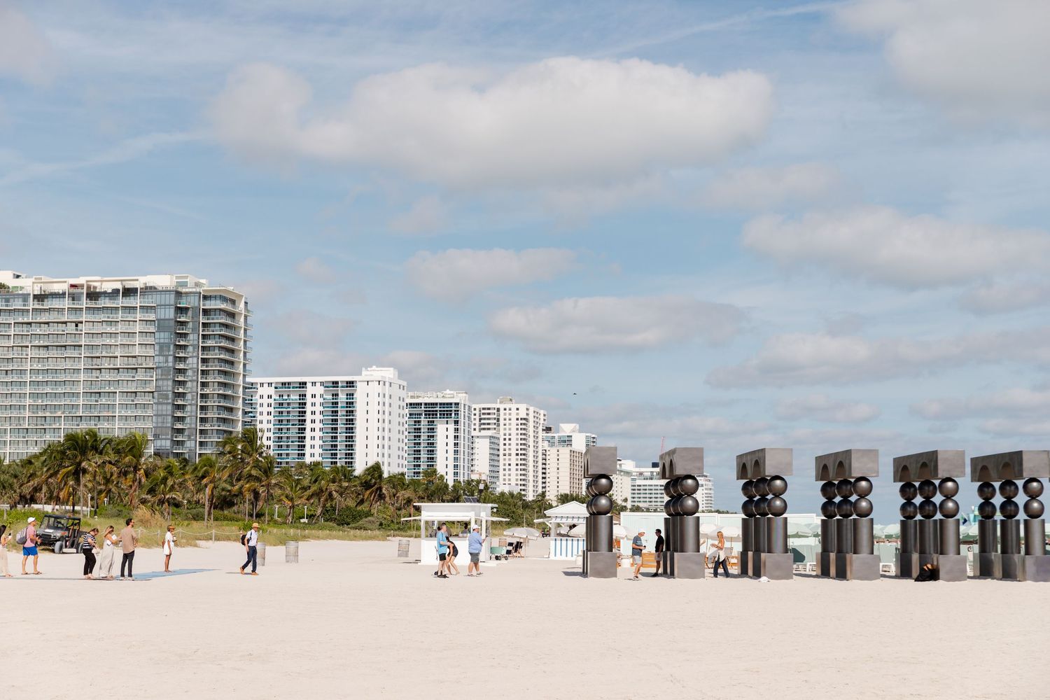 Panoramic view of Miami Beach with high-rise buildings, palm trees, and beachgoers enjoying the sandy shoreline.