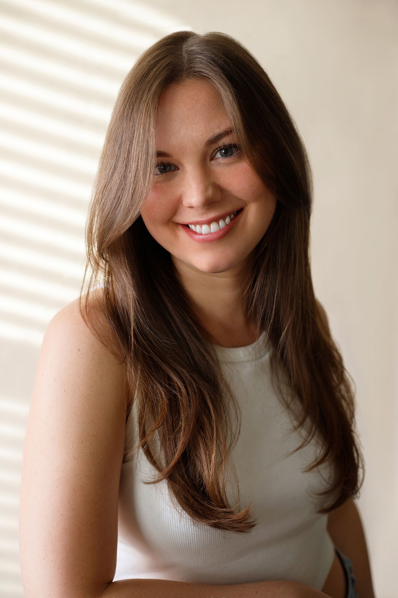 A person with long brown hair wearing a white sleeveless top smiles warmly in a series of four similar photos.