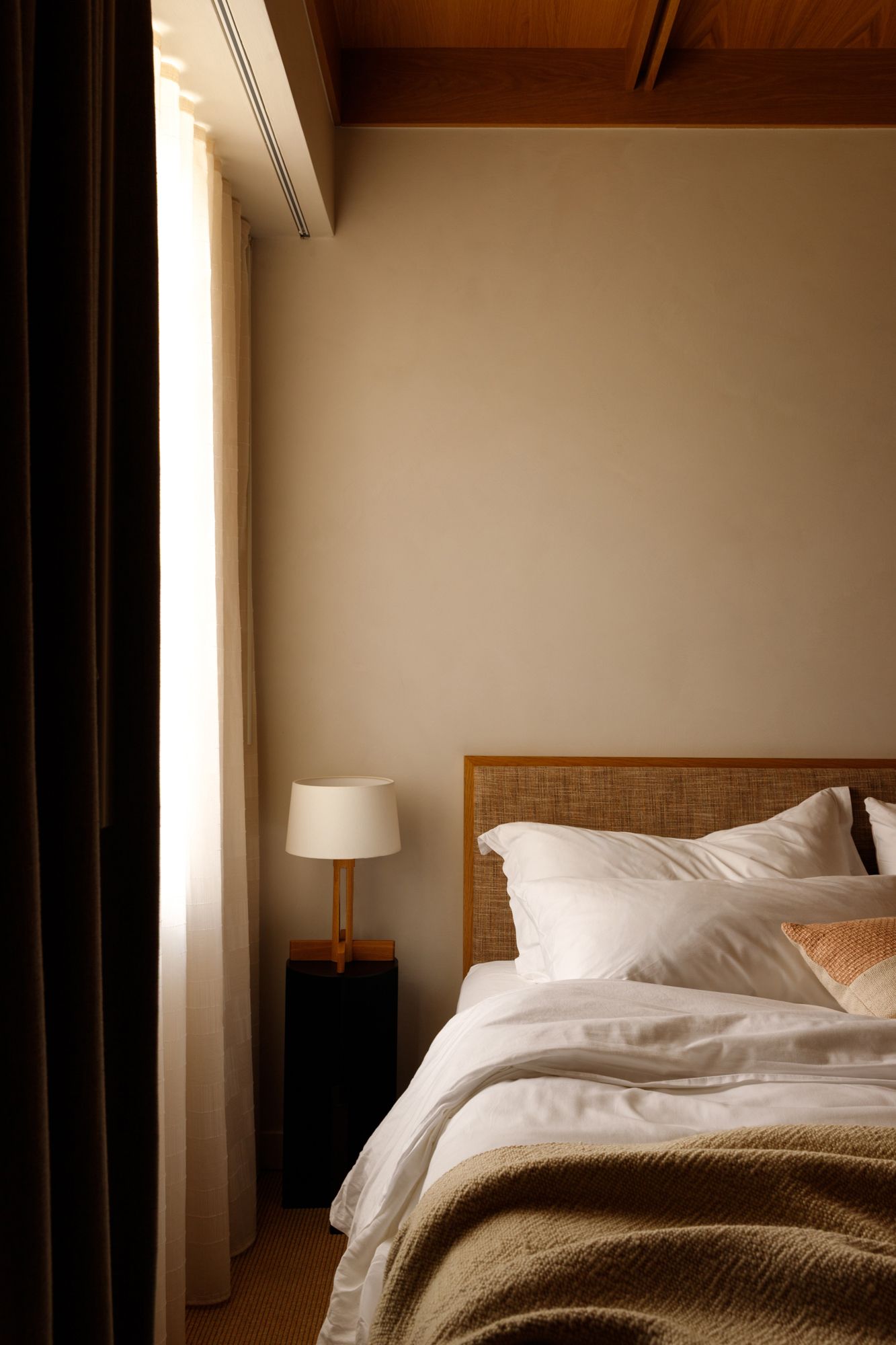 Cozy hotel bedroom with rattan headboard, white linens, and warm bedside lamp.