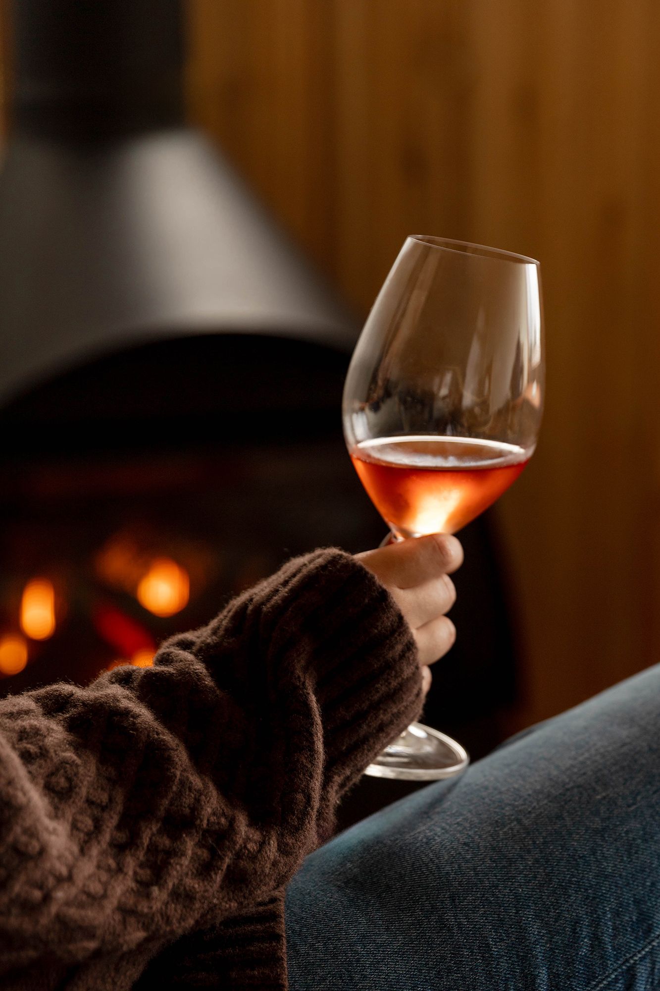 A glass of wine is held against a dark cozy background with warm ambient lighting creating a relaxing mood.