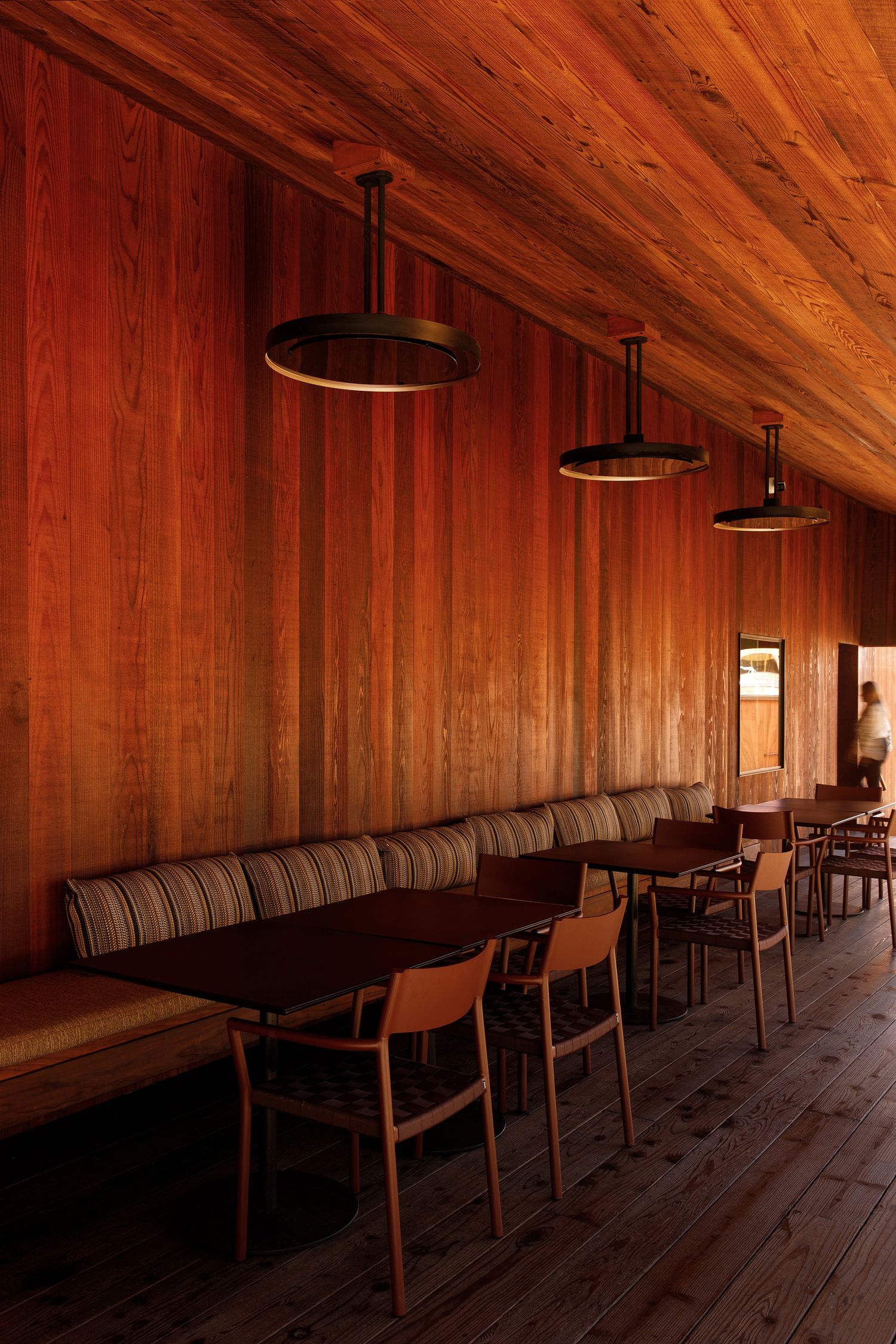 Warm wood-paneled restaurant interior with striped booth seating, pendant lights, and rustic wooden chairs and tables.