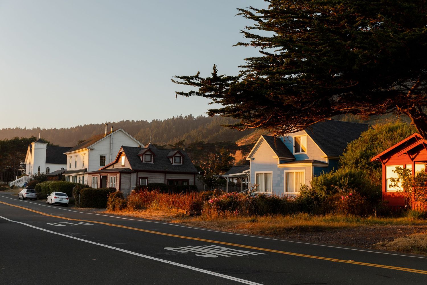 Row of coastal houses along a winding road at sunset with golden light illuminating their facades.