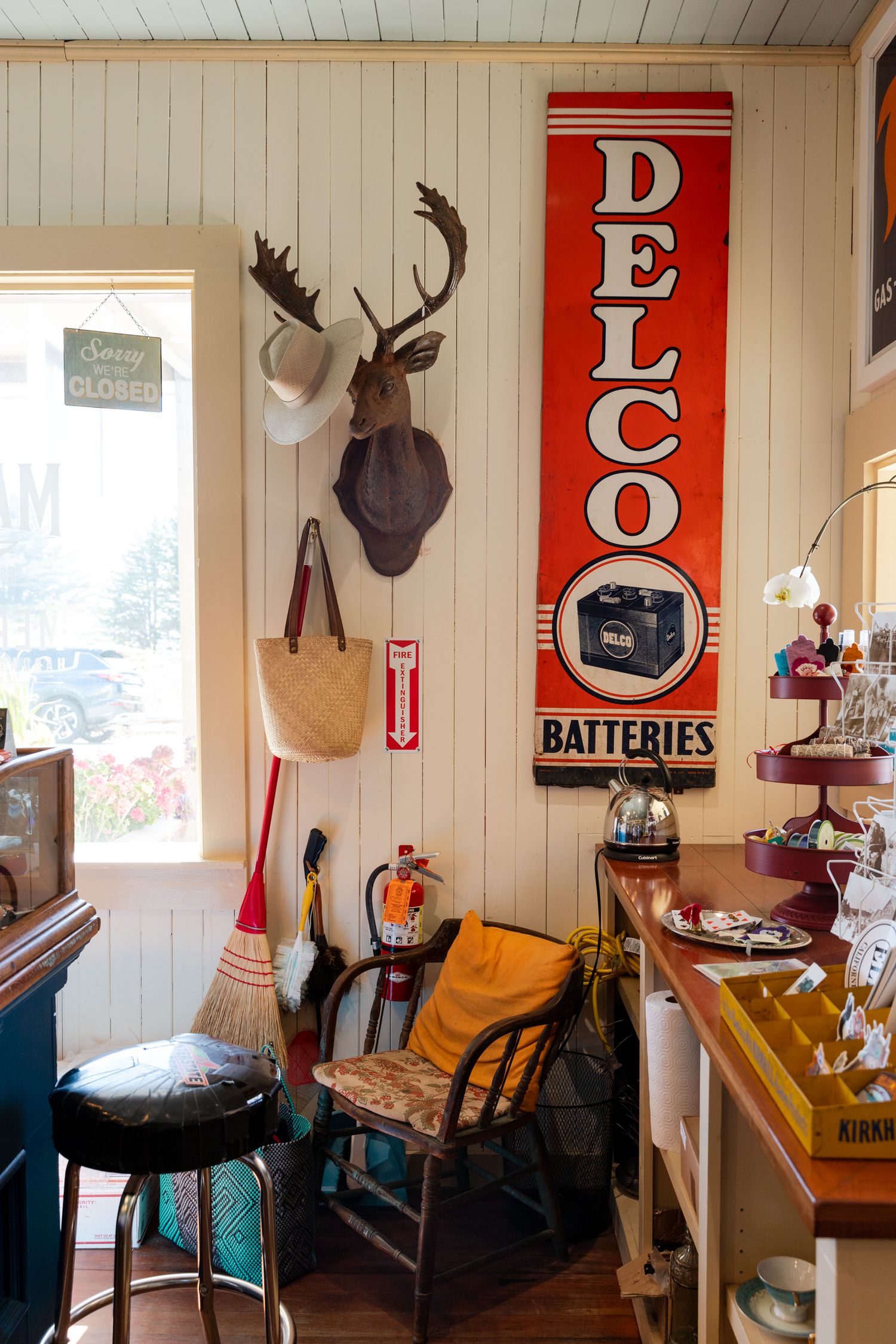 Vintage interior with mounted deer head and retro Delco Batteries sign on white paneled wall.