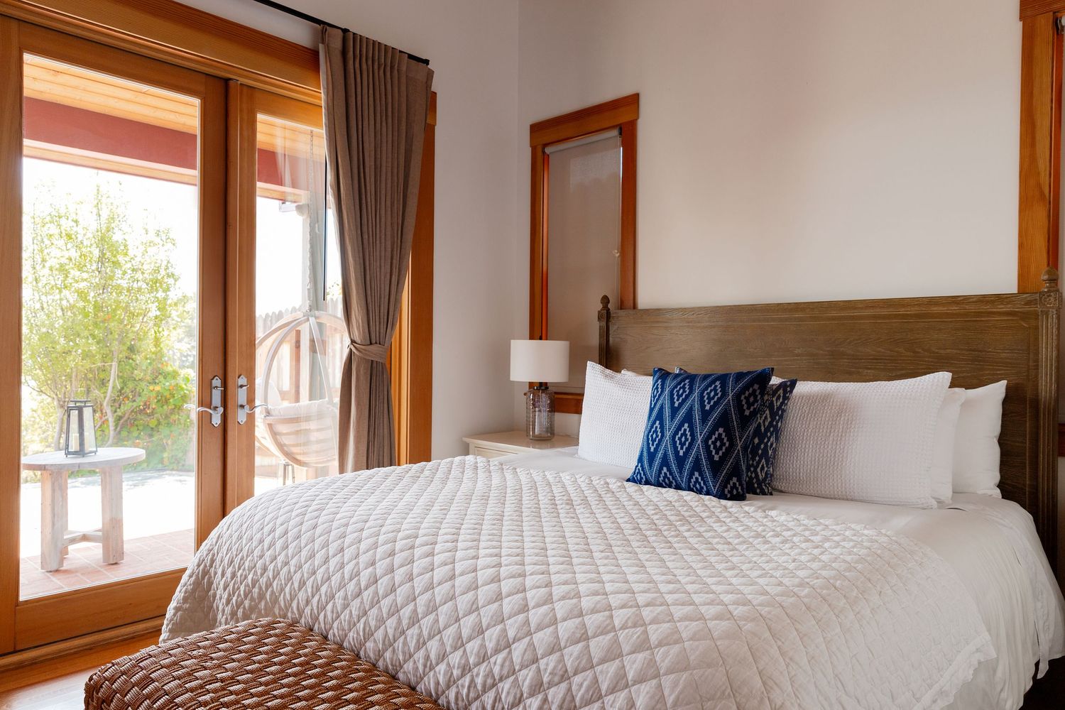 A bright modern bedroom with white bedding, wood trim windows, and a navy blue accent pillow.