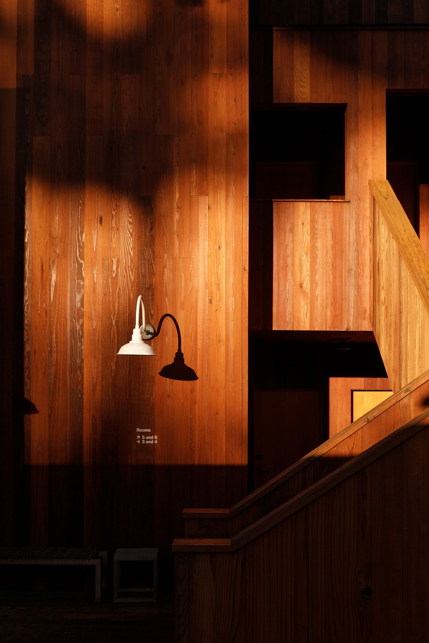 Warm wooden interior wall with a white gooseneck lamp casting light near a staircase railing.