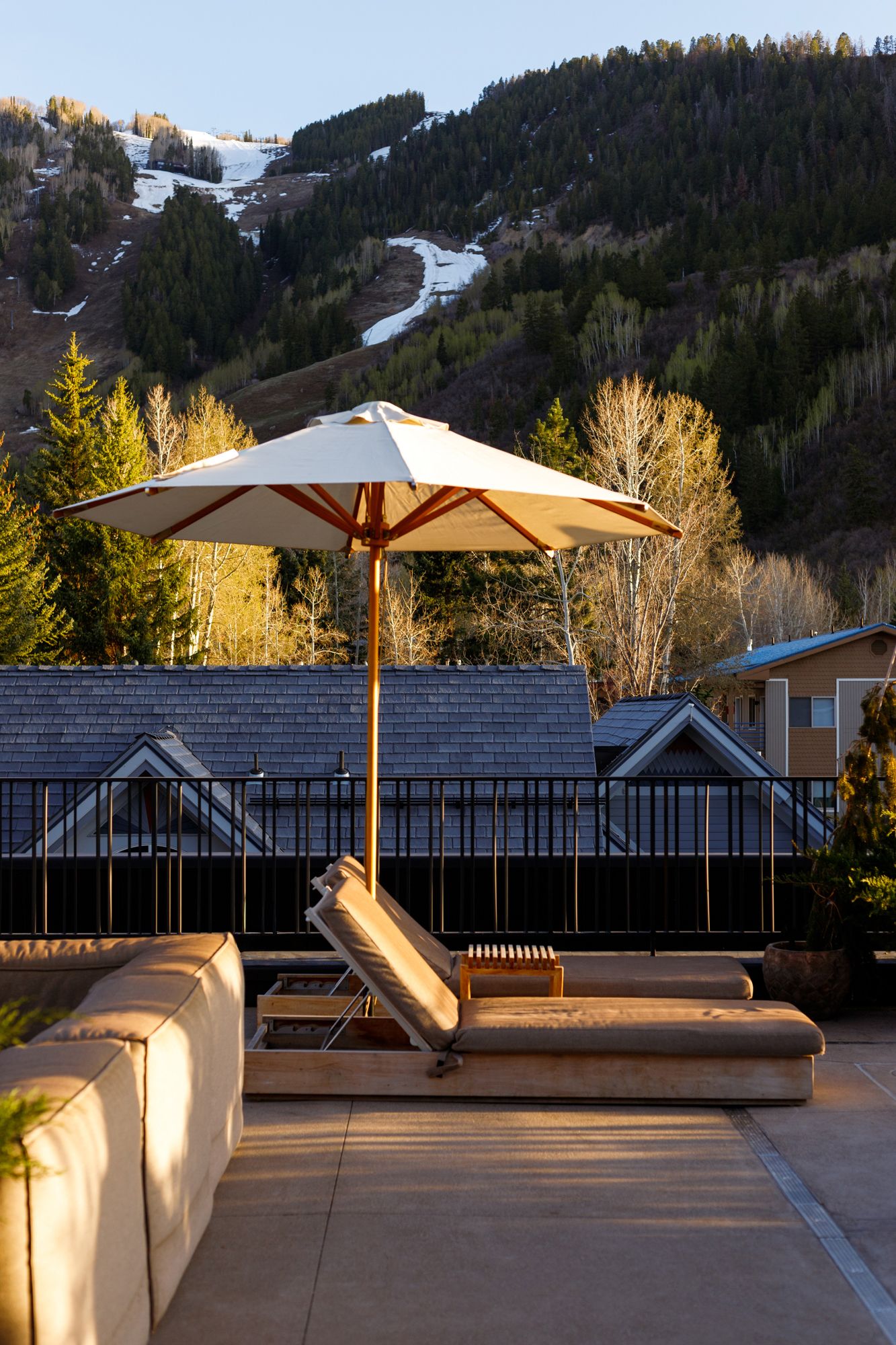 Rooftop terrace with lounge chairs and white umbrella against snow-dusted mountain backdrop.