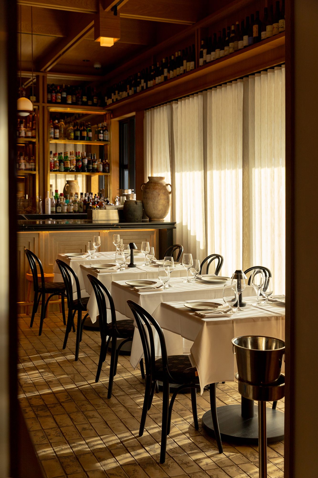 Elegant restaurant interior with white-clothed tables, black chairs, and a well-stocked bar.