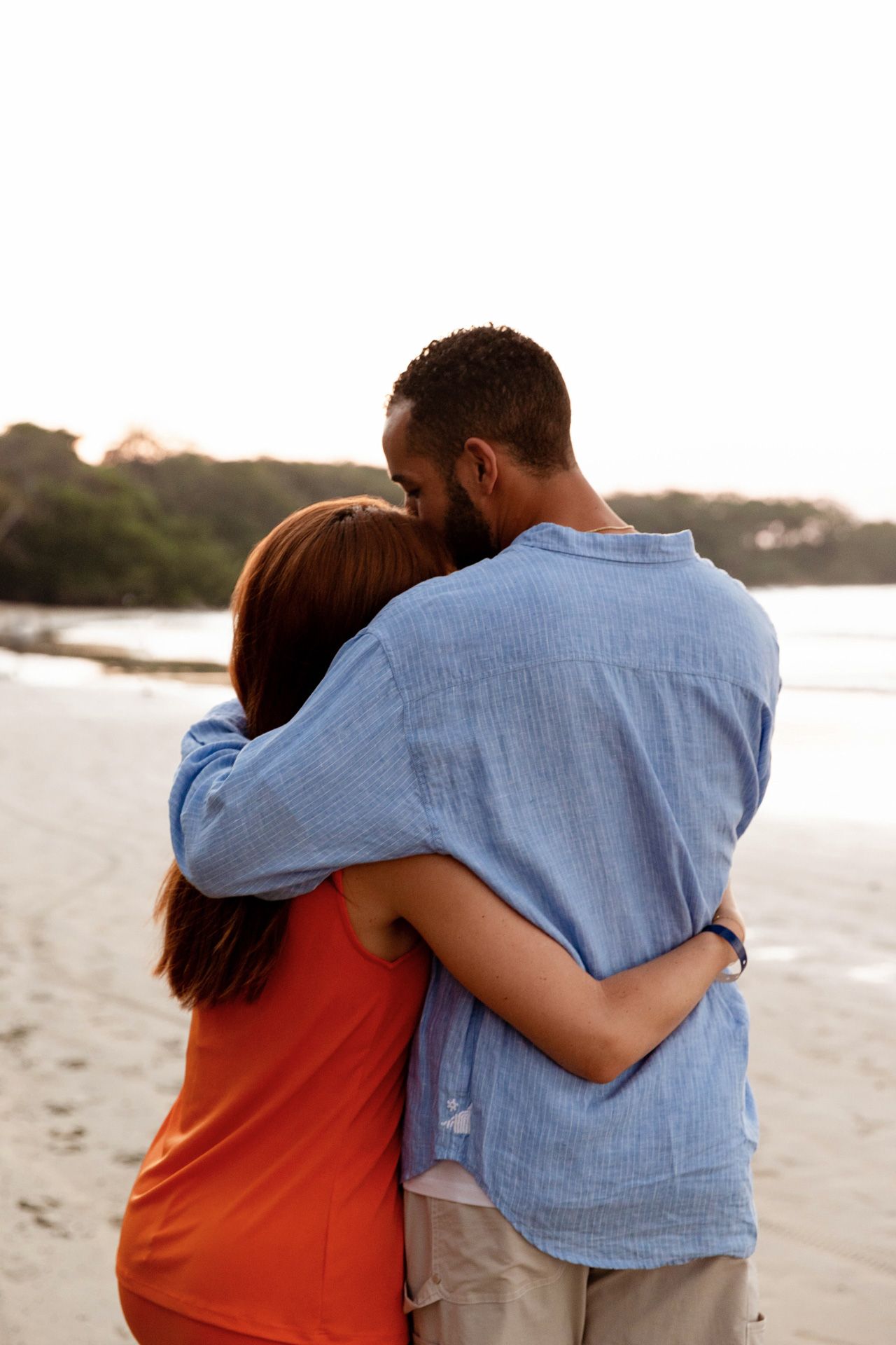 A couple in casual attire sharing an intimate embrace on a beach during golden hour.