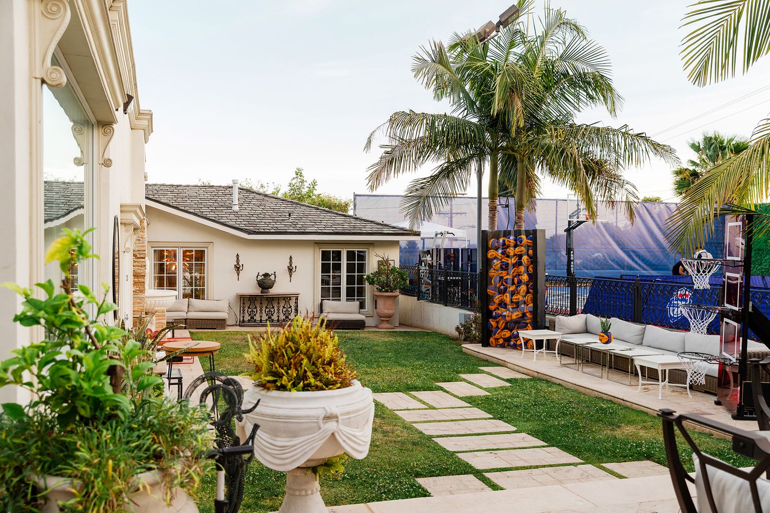 A panoramic view of a modern backyard patio with palm trees, outdoor furniture, and stone pavers creating a resort-like atmosphere.