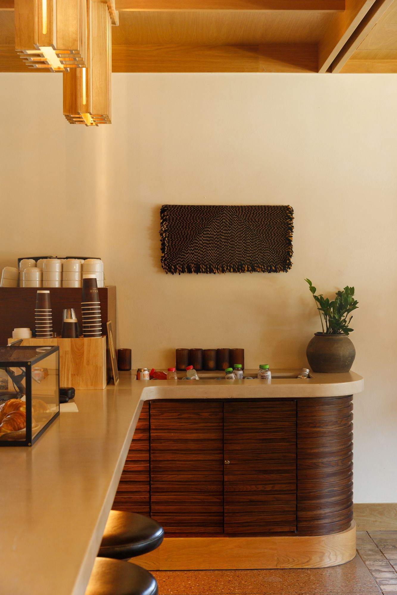 Warm hotel cafe counter with wood cabinetry, decorative wall art, pendant lights, and coffee station.