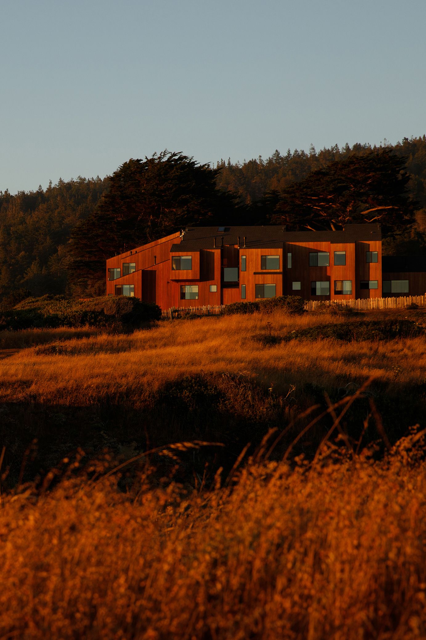 Red building at golden hour surrounded by dry grass fields and dense forest trees under a clear sky.
